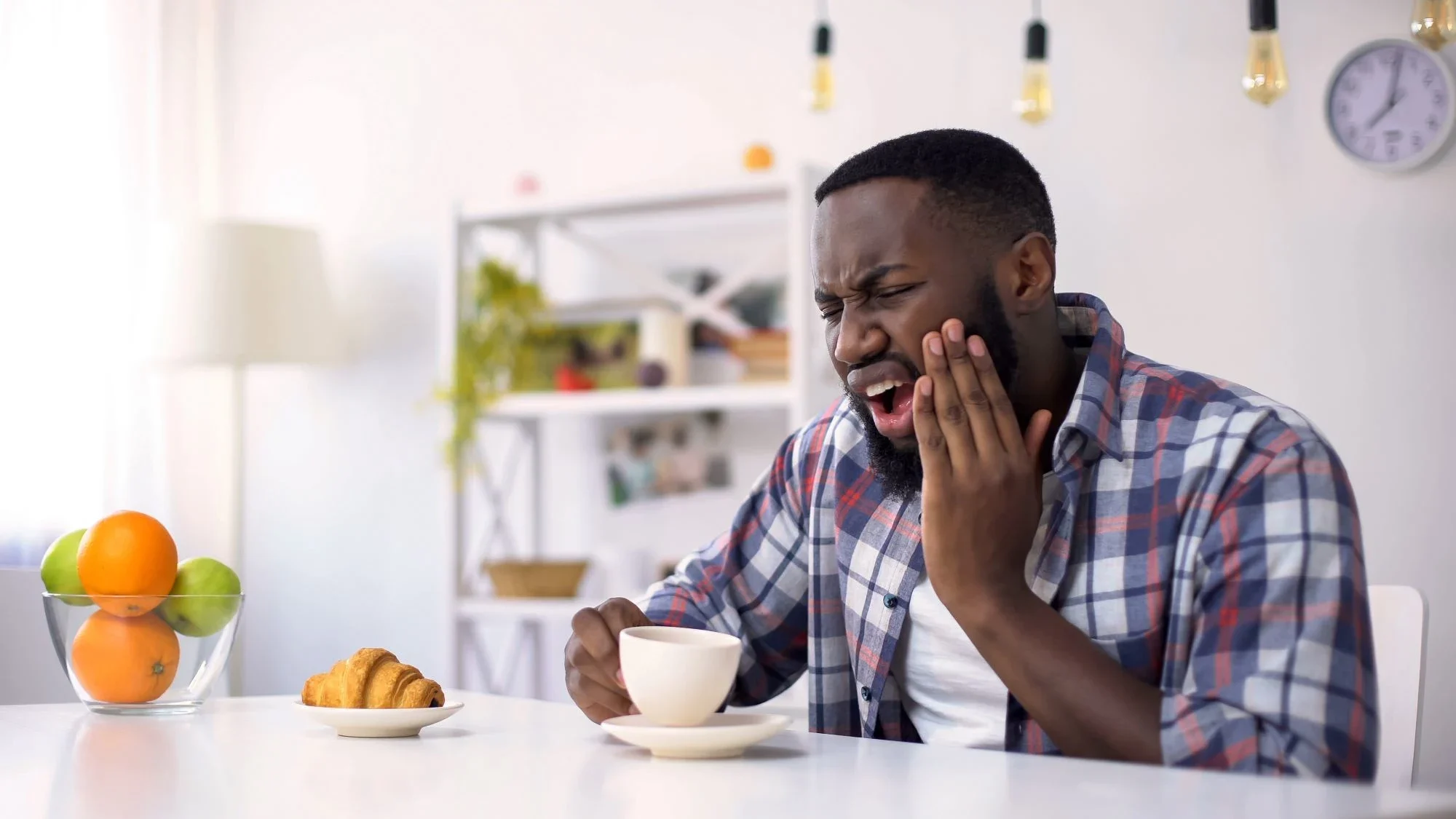 Man wincing in pain after sipping hot coffee with sensitive teeth 
