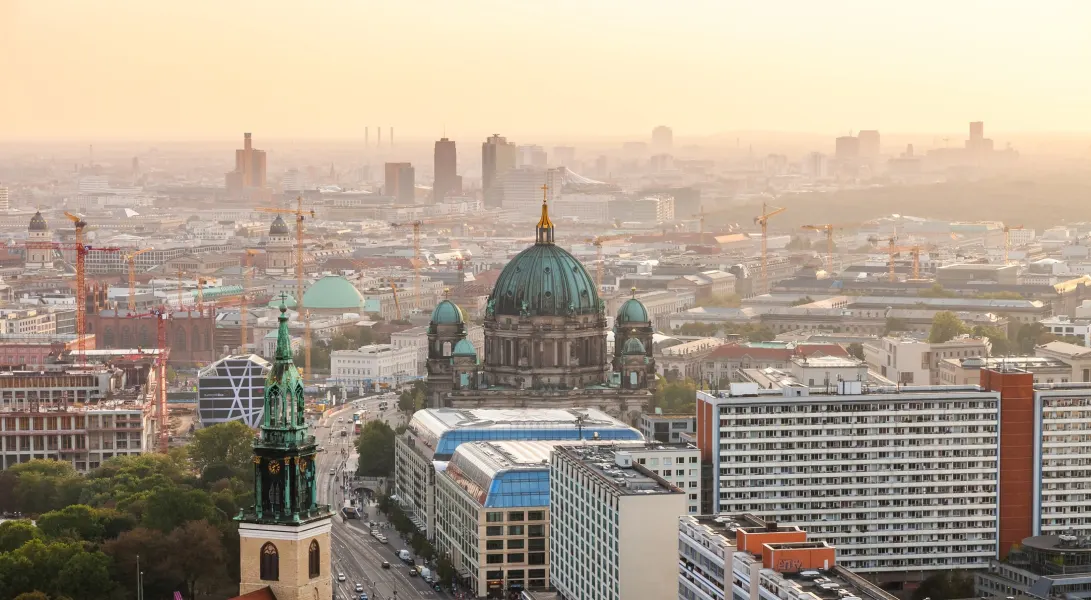 Hier sehen Sie ein Bild von der Stadt Berlin aus der Vogelperspektive. Im Zentrum des Bildes ist der berliner Dom zu sehen. Es ist Sonnenuntergang.