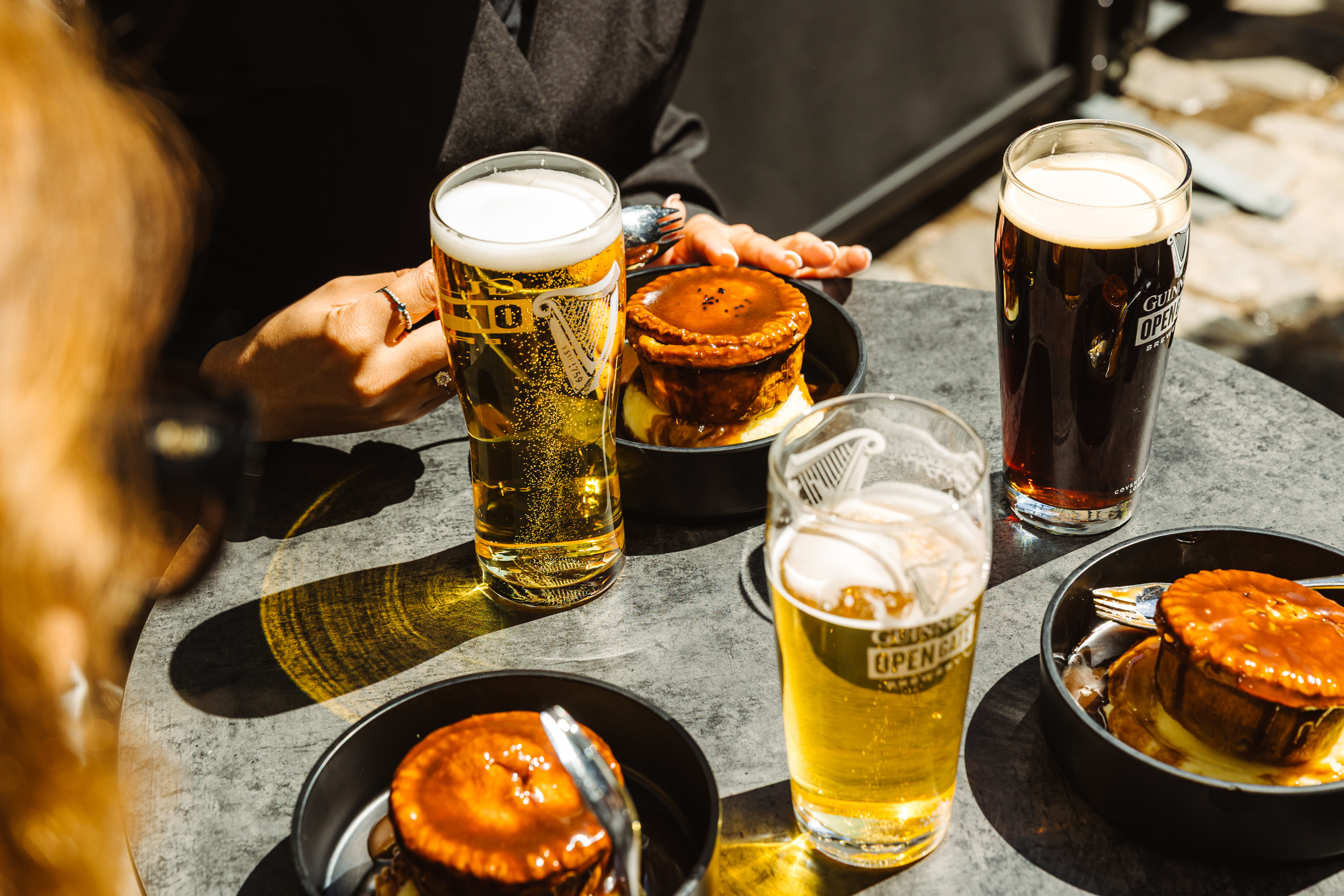 3 pints of beer sparkle in the sun in the outside beer garden at the Guinness Open Gate Brewery London