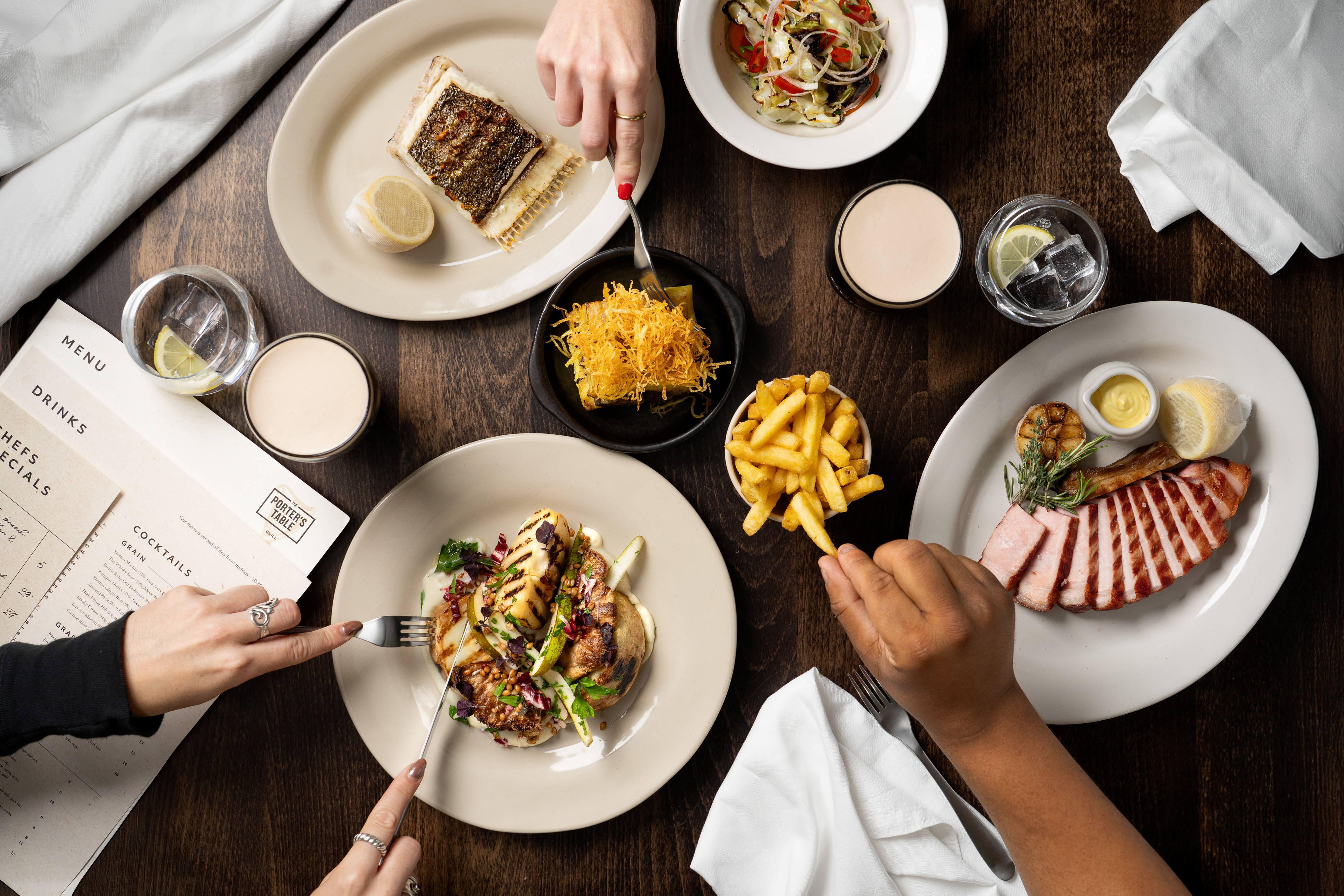 Food on the table, people are reaching for fries and fishes on plates.