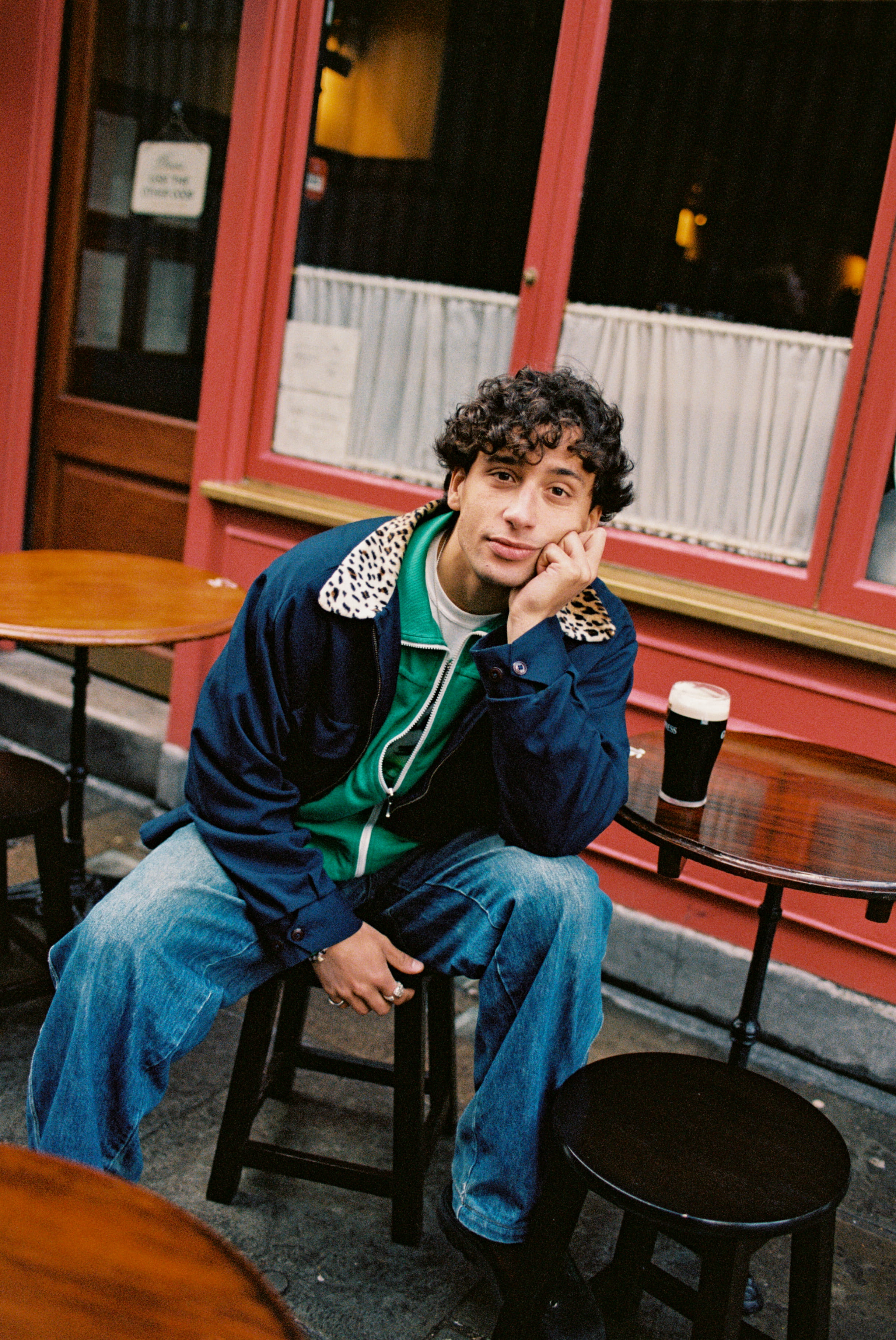 Dublin-based rapper, Khaki Kid, sits outside on a pub stool with his face rested on his hand and a pint of Guinness sitting beside him on the table.