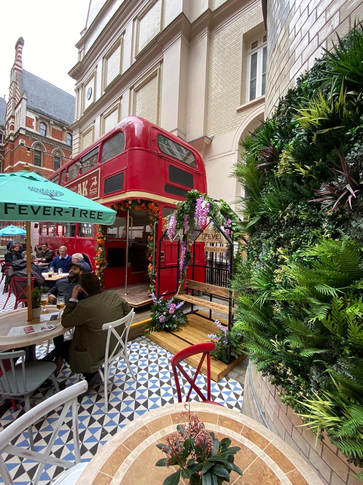 The outside drinking area in The Old Bank of England pub in Central London complete with a red London bus, and parasol covered tables and chairs.
