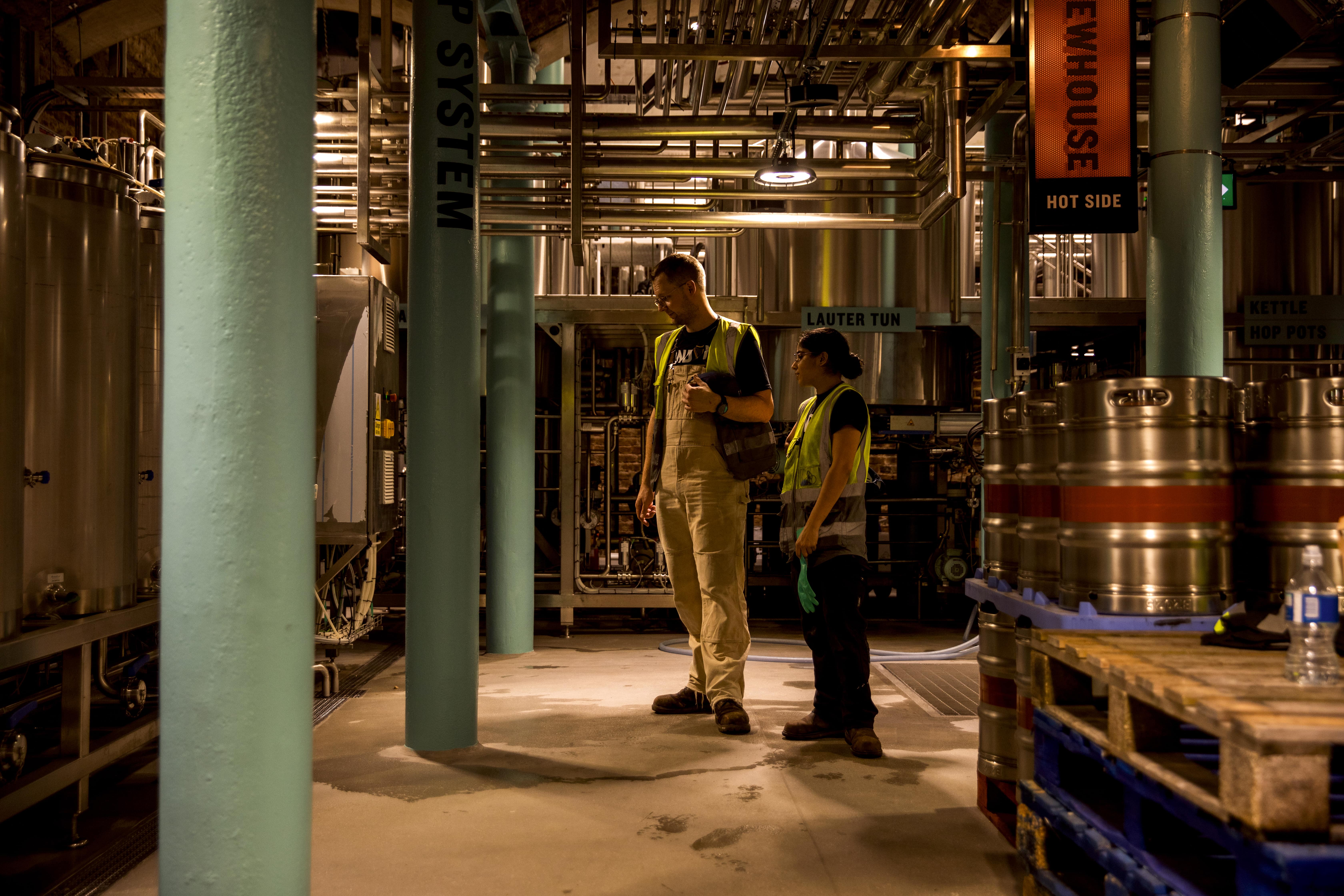 Two brewers stand in the micro-brewery at Guinness Open Gate Brewery checking equipment.