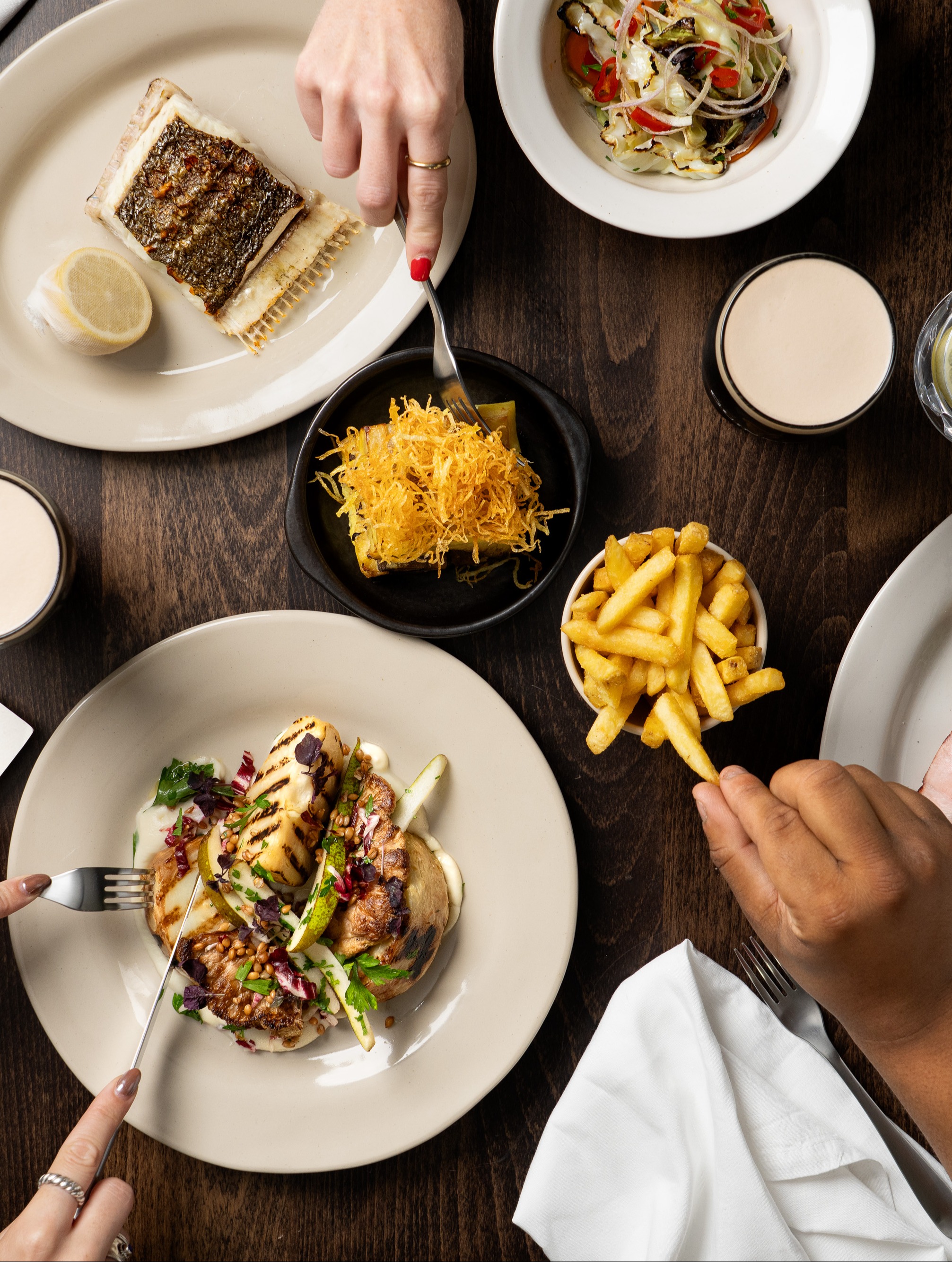 Food on the table, people are reaching for fries and fishes on plates.