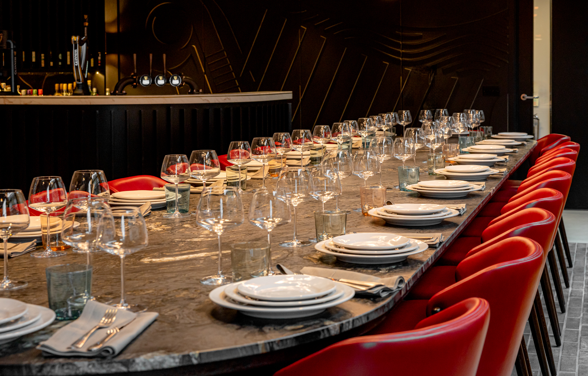 A long black marble table with red leather chairs with plates, cutlery and wine glasses set on the table