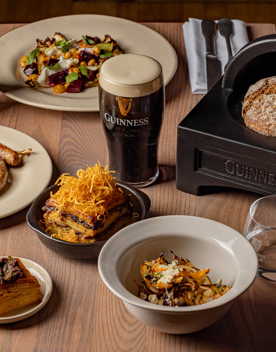 An image of food on a table. Guinness glass with poured Guinness on the middle and the bread in Guinness haversack