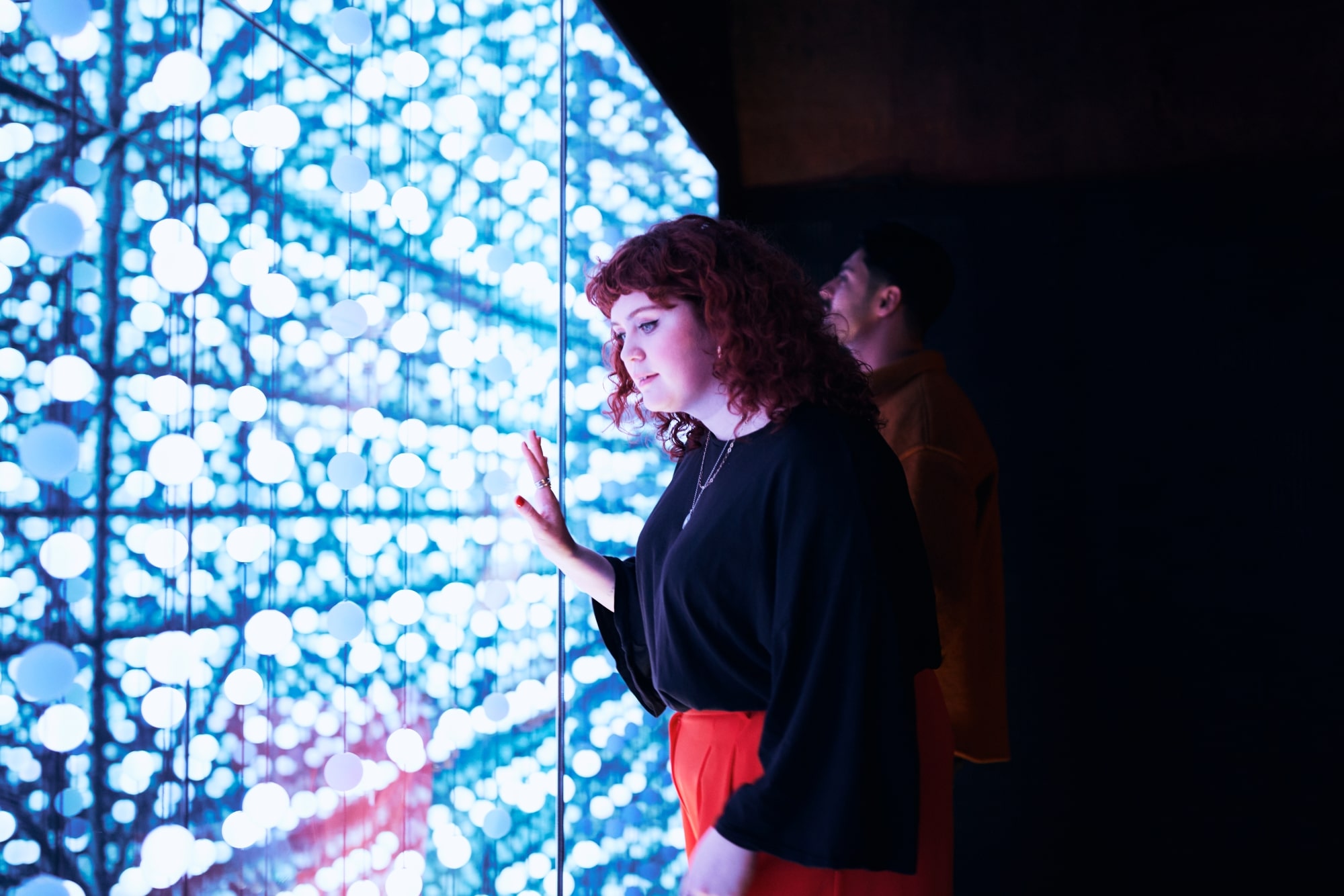 A woman leans on a brightly lit wall.