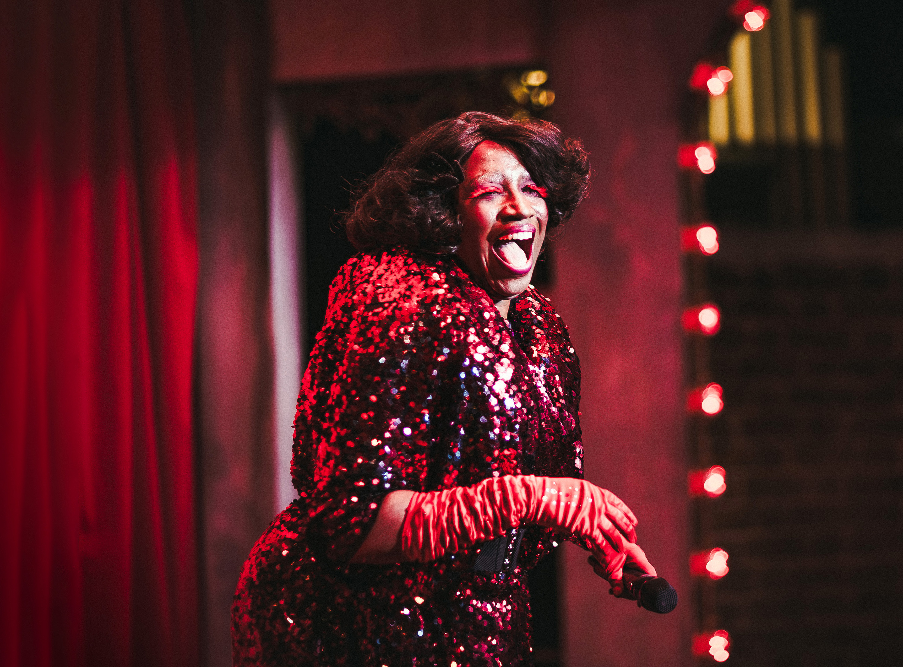 A woman performs comedy on stage in a glittering red outfit in Central London