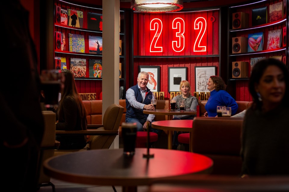 A man and three woman sit comfortably in one of the cosy booths and under the neon red BAR 232 sign, as they drink their pints of Guinness.