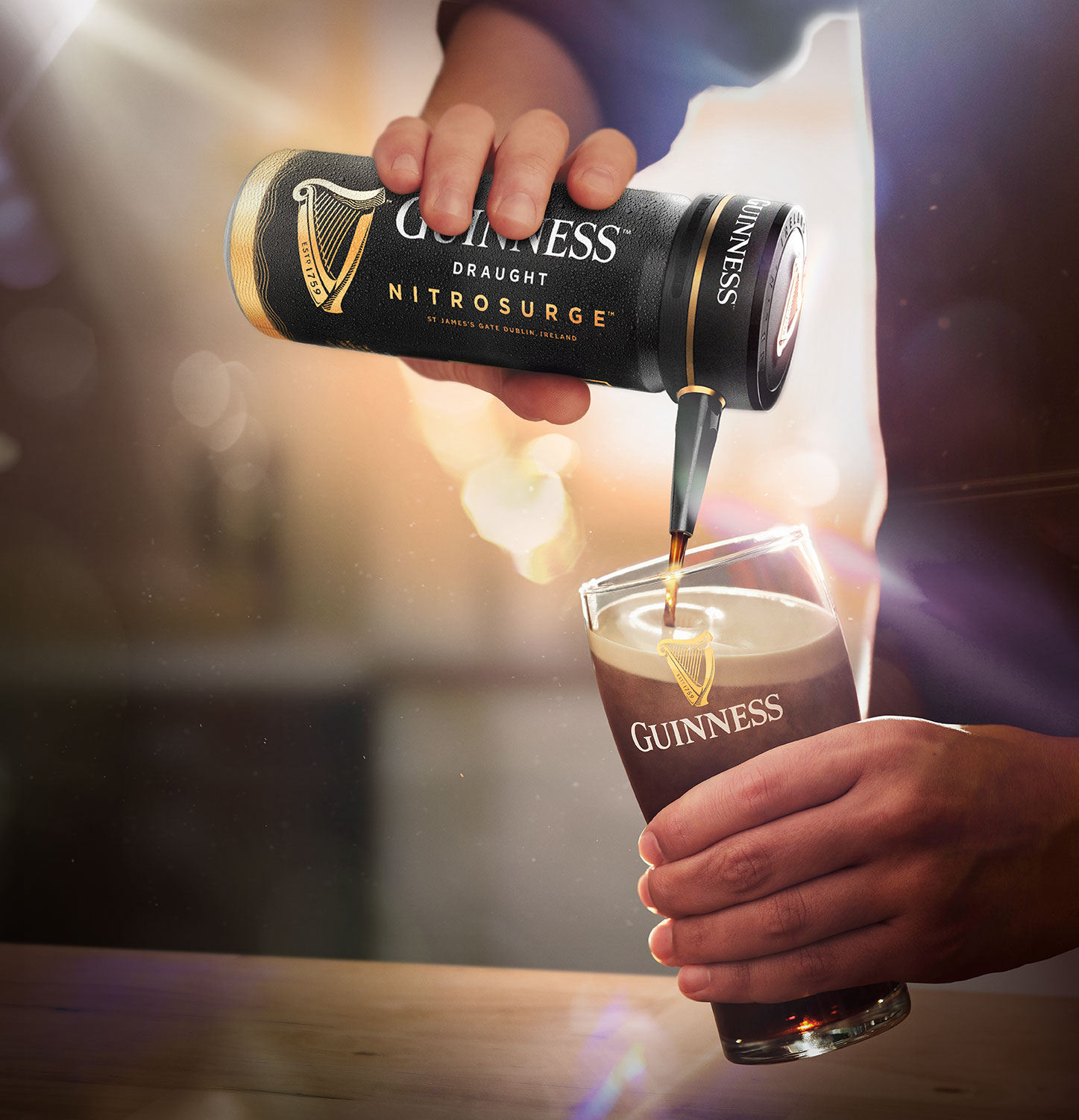 A hand pours Guinness from a Nitrosurge device into a branded glass, creating a creamy head. 