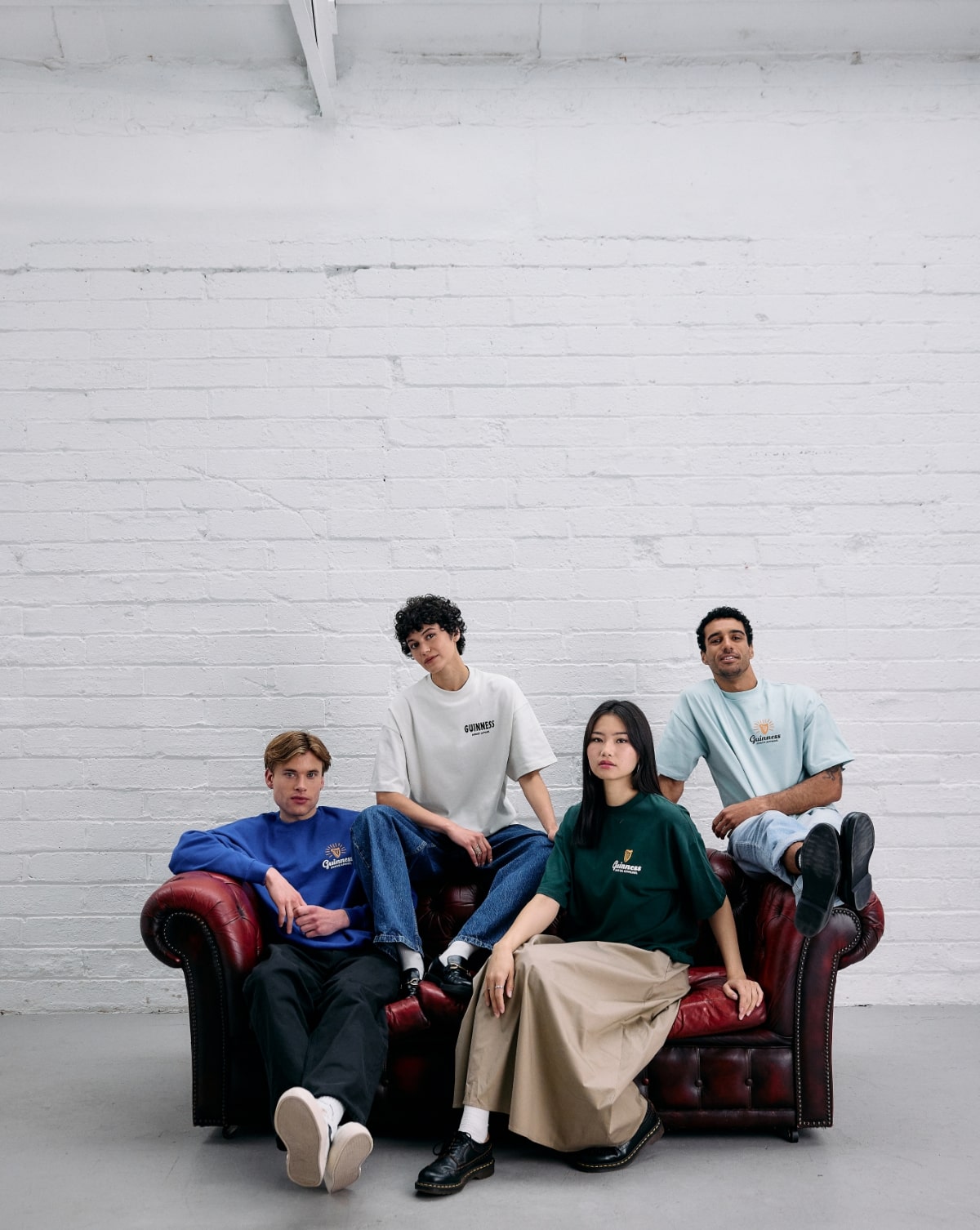 Four young people pose on a brown sofa, wearing Guinness branded casual clothing. 