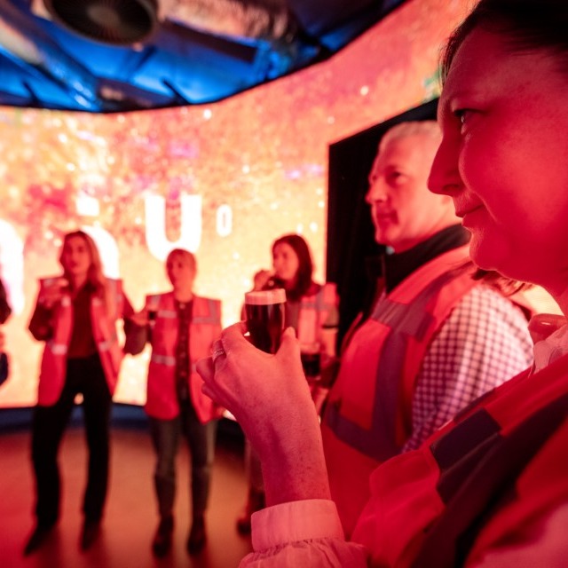 A man and a woman stand with their backs to the camera. They are facing a bright, neon "232°C" sign on a wall.