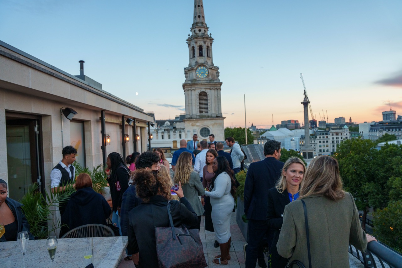 People stand at an event in Kitty Hawk's rooftop bar and restaurant in Central London with views overlooking London's Trafalgar Square.