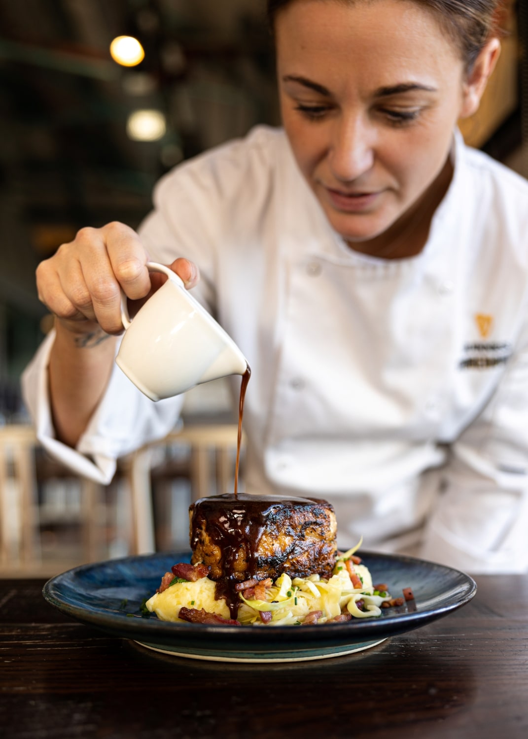 A chef pours gravy over a plate of food.