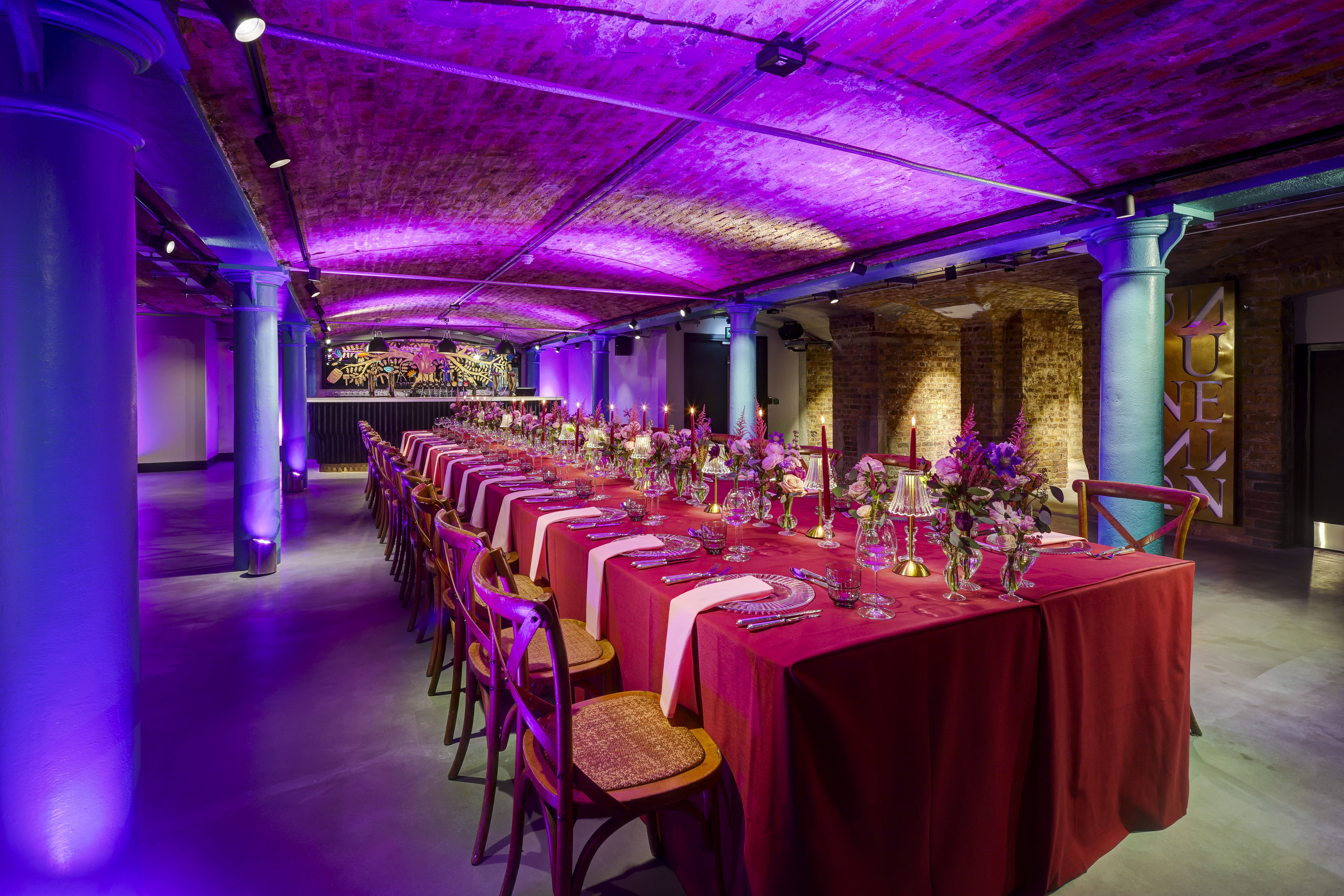 A long table dressed with candles, flowers, and fashionable tableware run in the centre of the Guinness events space lit with ambient lighting.