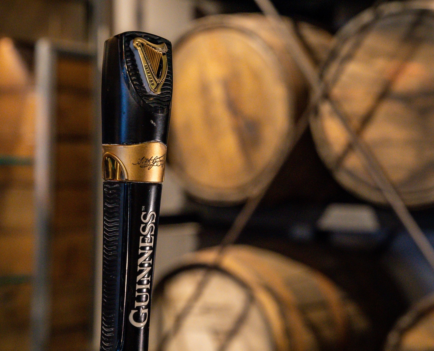 A Guinness branded beer tap with wooden barrels visible in the background.