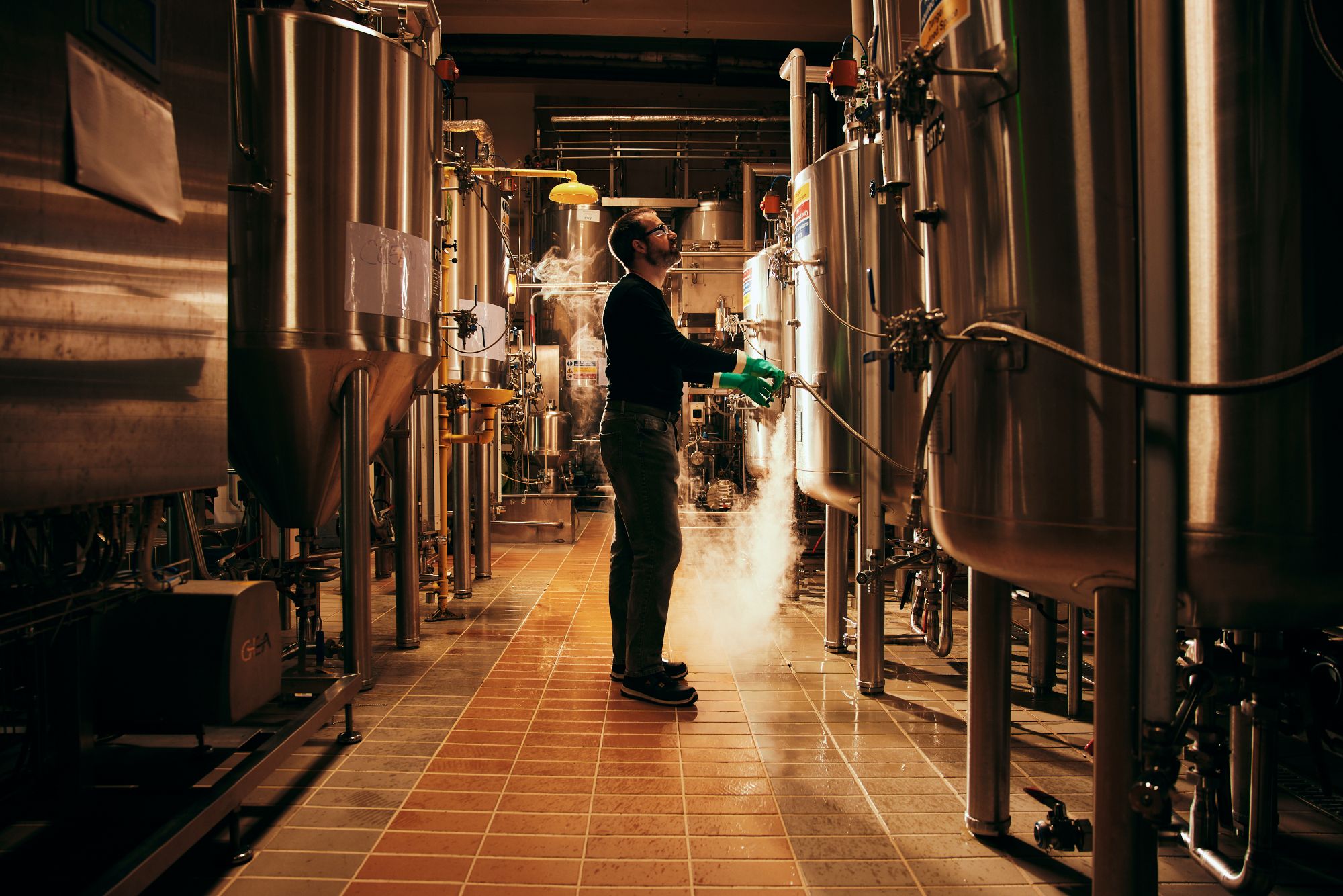 A man stands among beer fermentation vessels in a brewery.