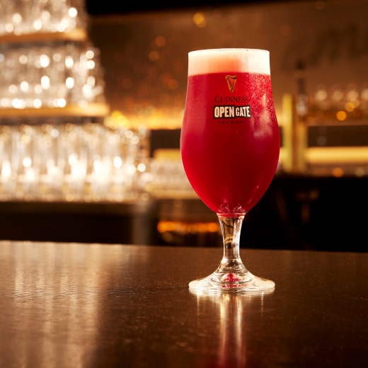 A pint of bright red beer on a bar in a Guinness branded pint glass with a stem.