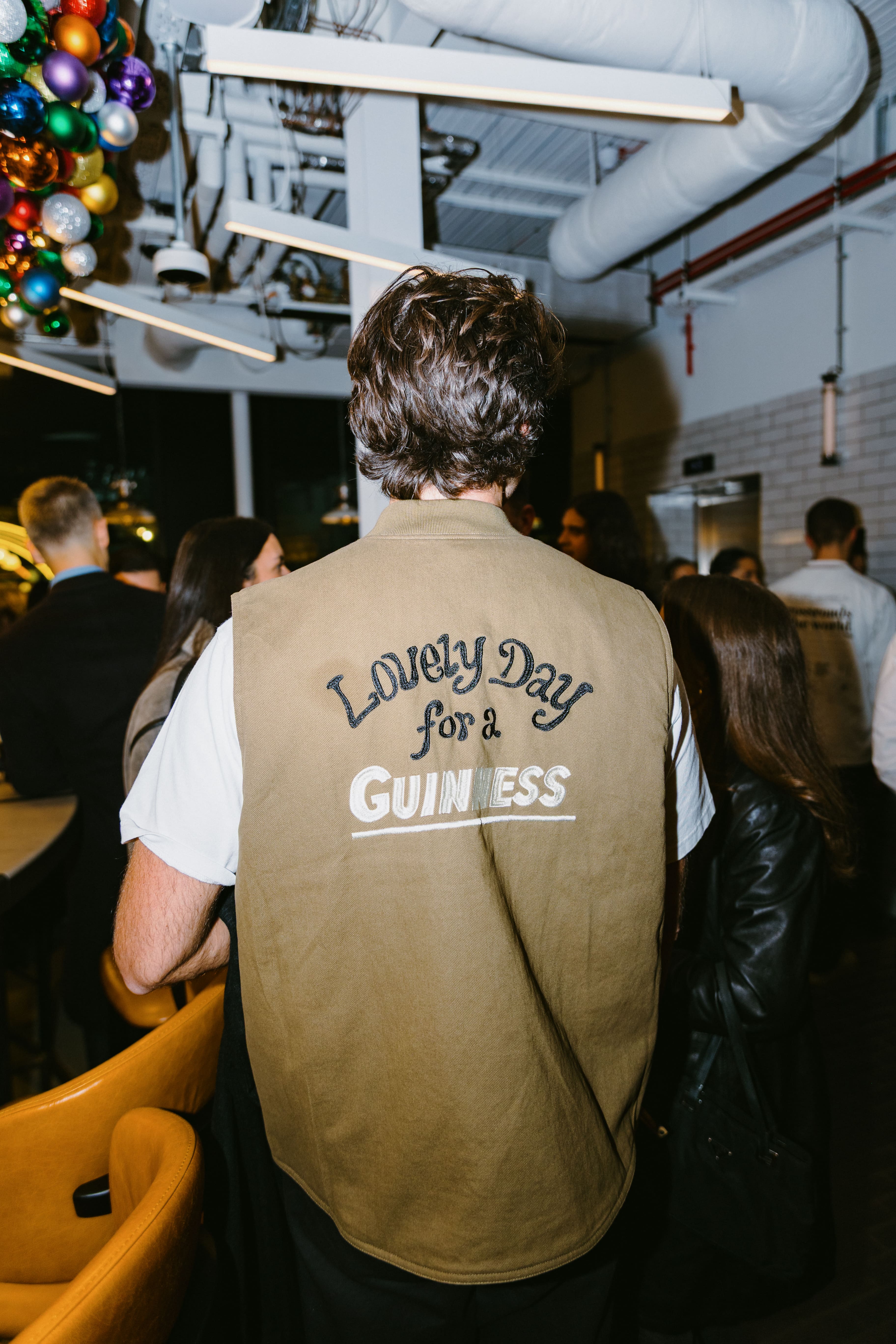 A man in a bar with his back to the camera wearing a Guinness vest
