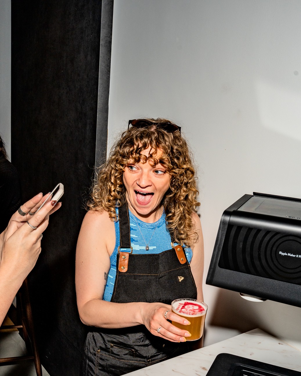 A girl holding a short drink with an image printed ontop of the foam and smiling as someone takes here picture