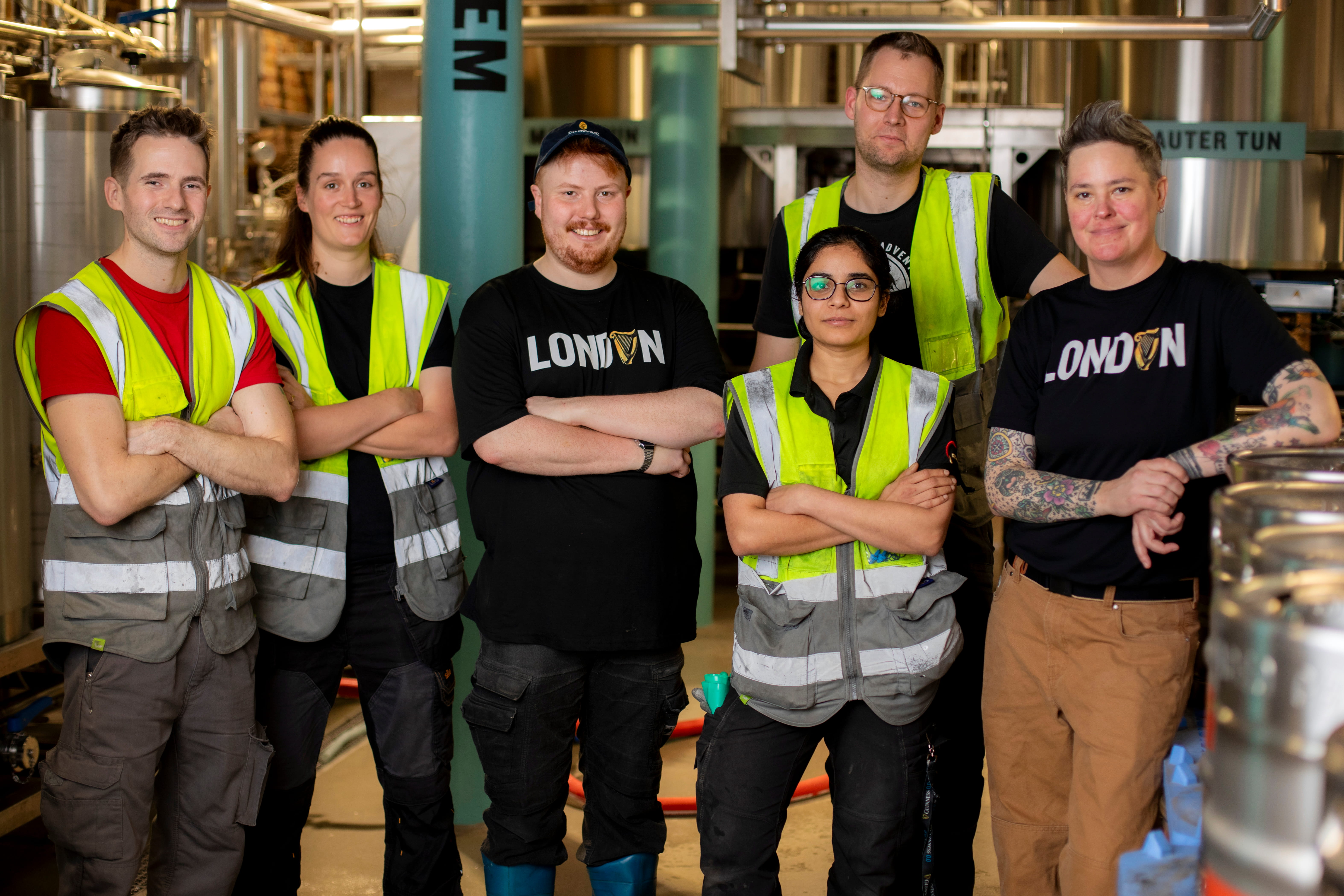 A group of brewers standing in the brewery posing for a group picture all wearing Guinness clothing