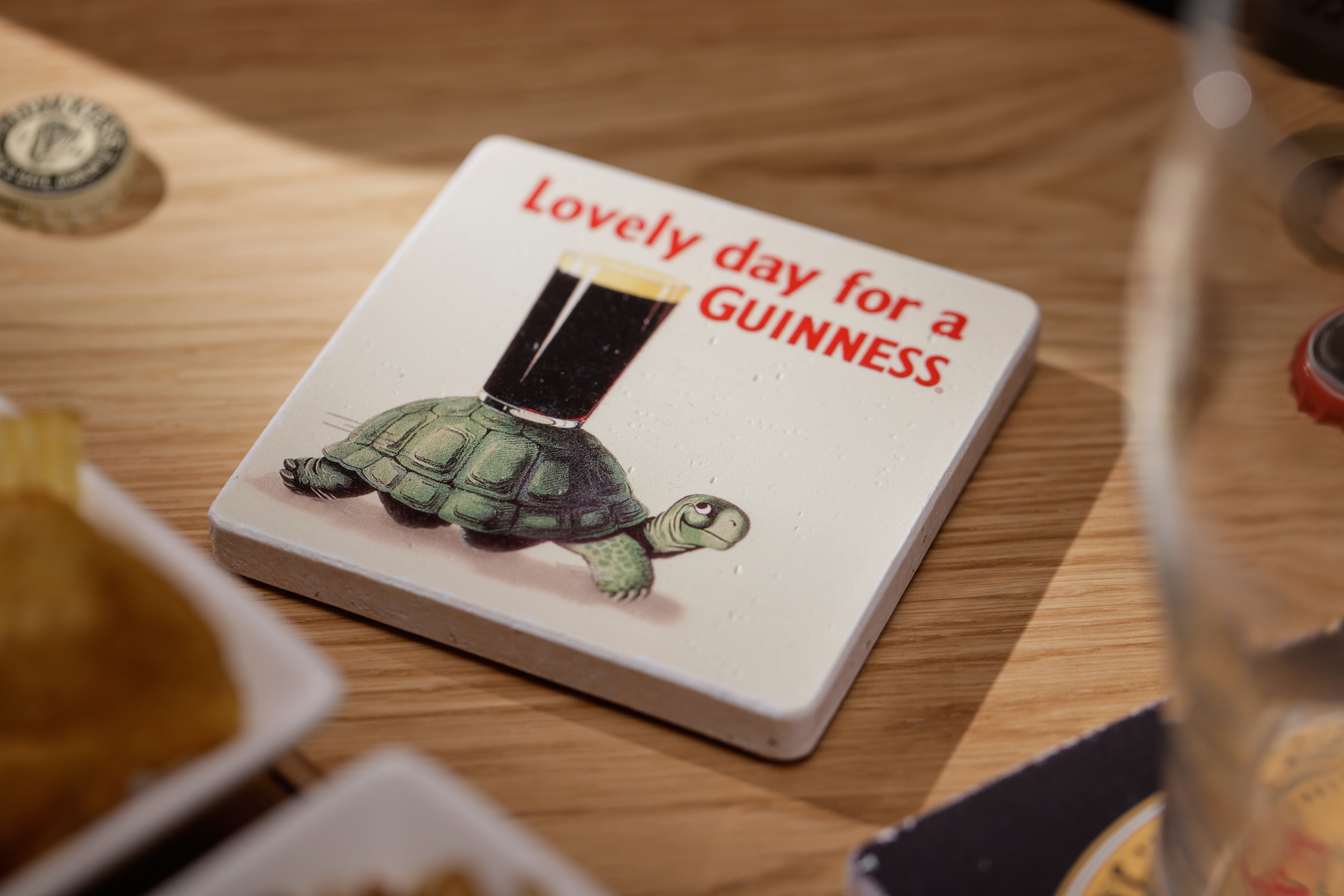 A brown wooden table with a ceramic beer mat with Lovely Day for a Guinness written on
