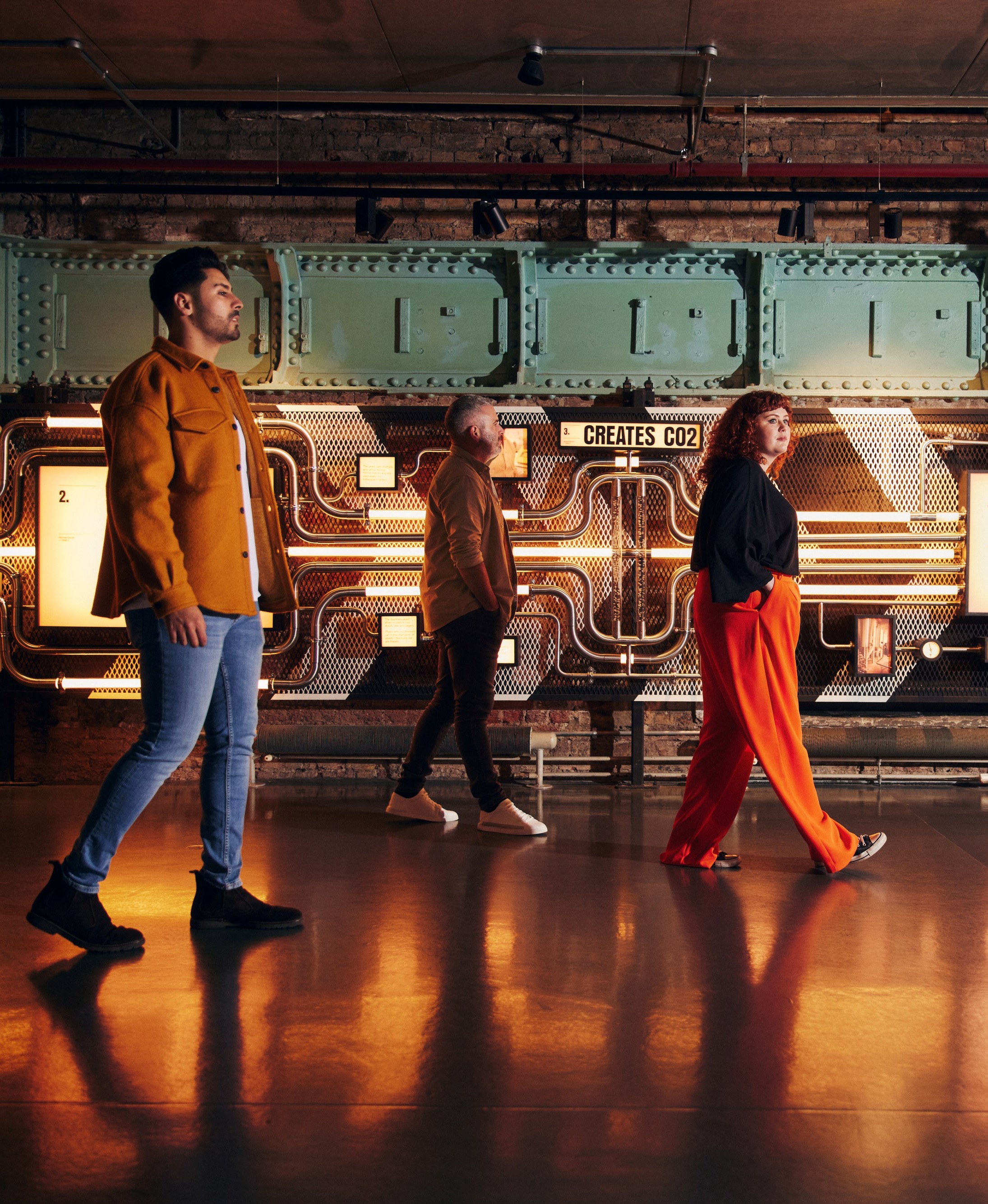 3 people going along the room in Open Gate London. Sign with the text "Creates CO2"