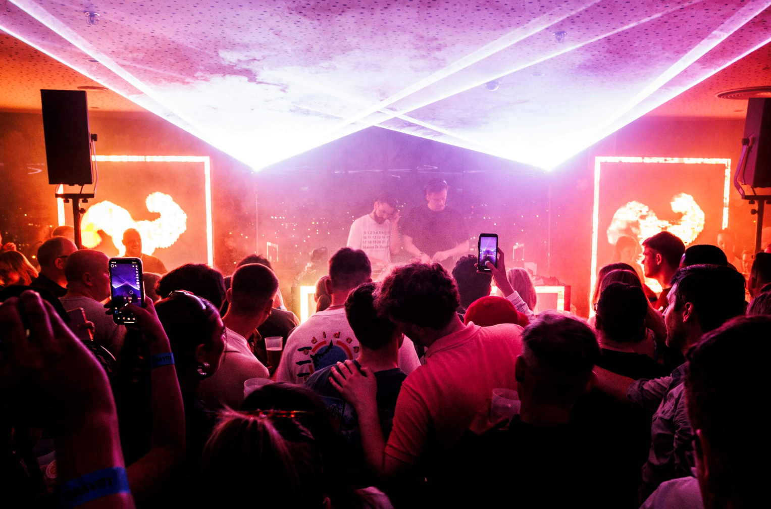 People dance to a live DJ set in the underground events space at Guinness Open Gate Brewery London, with speakers and laser show lighting.