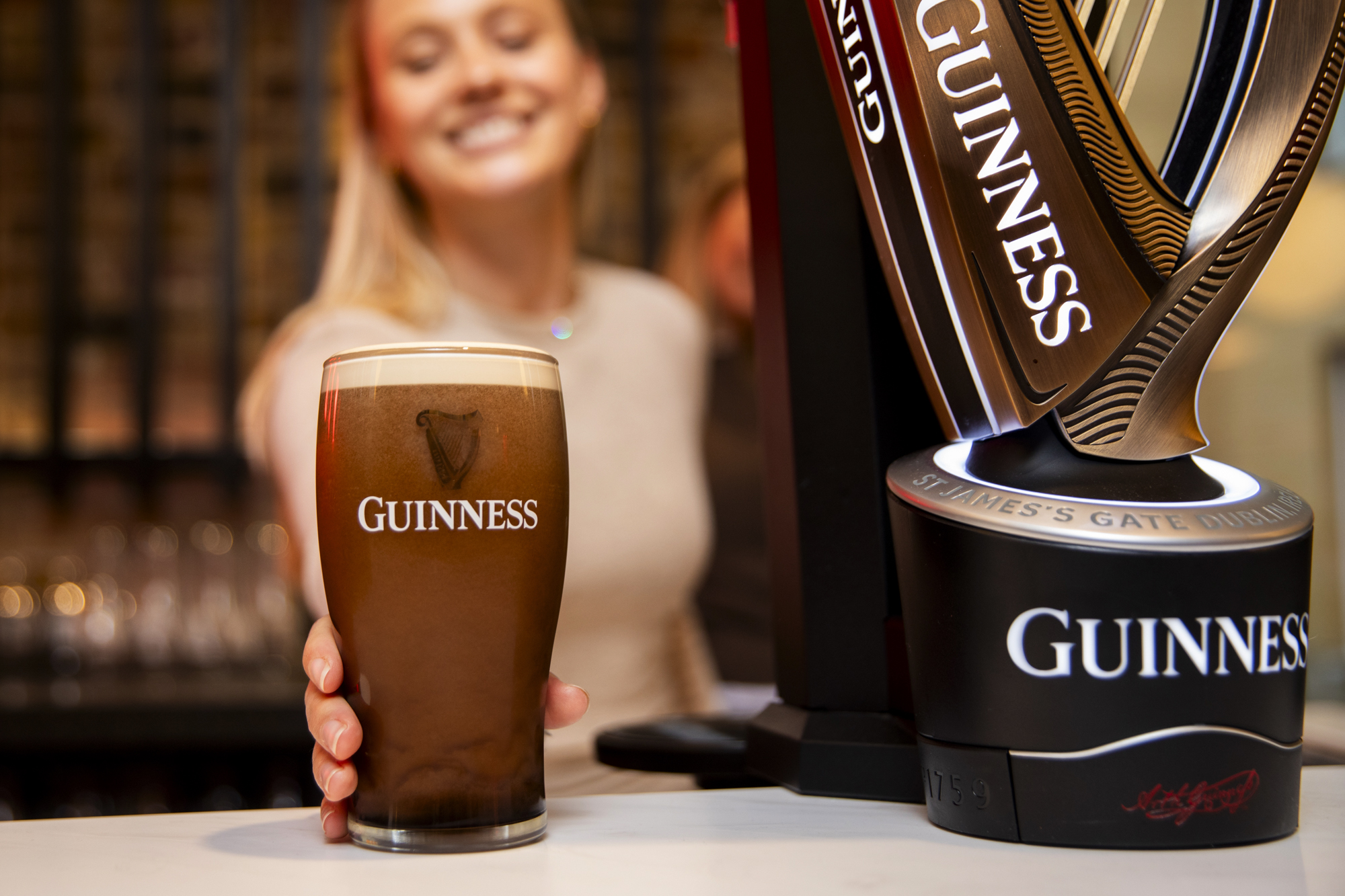 A woman putting a pint of Guinness down onto the bar after just pouring it