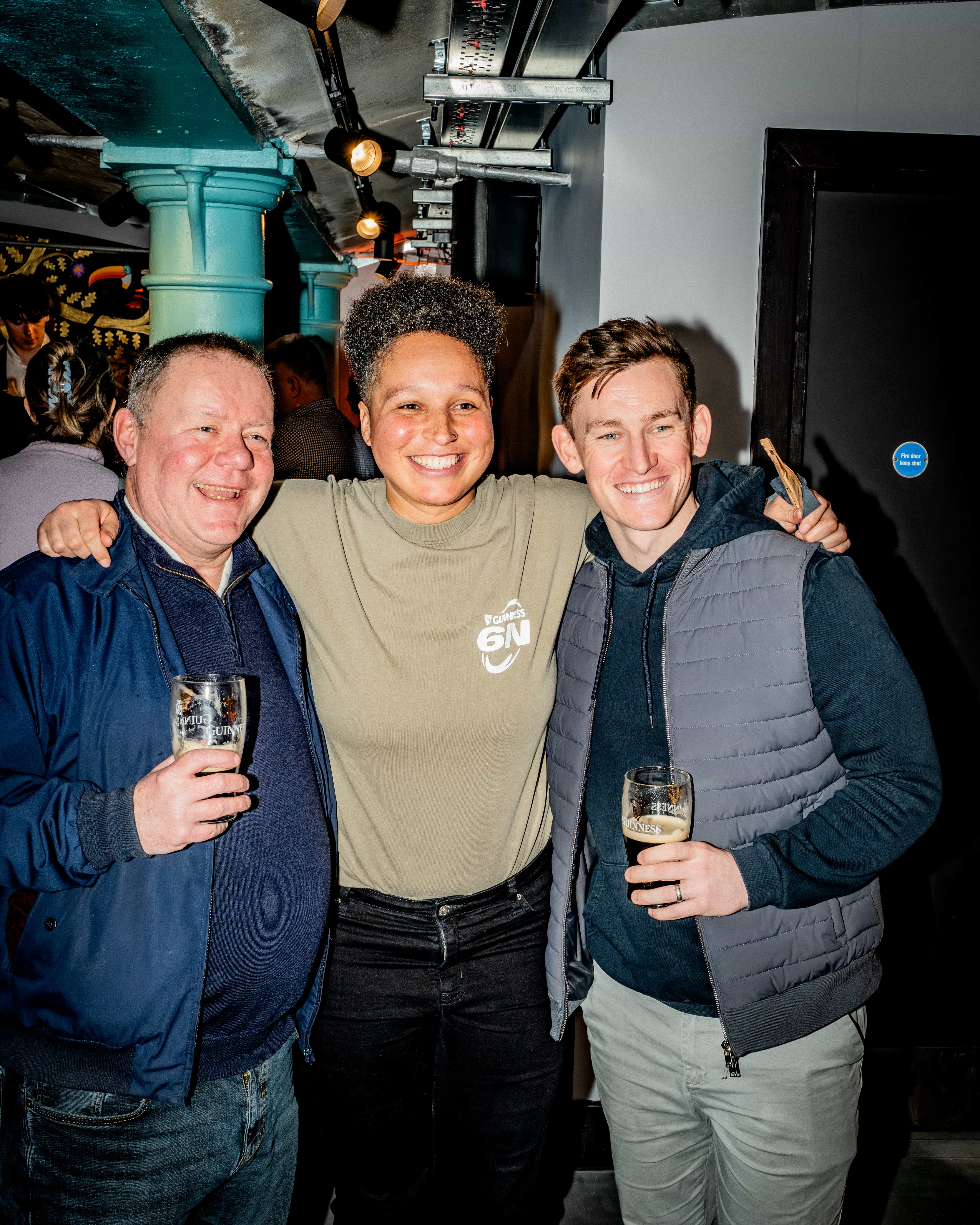 Three people posing for a photo in a bar while holding pints of Guinness