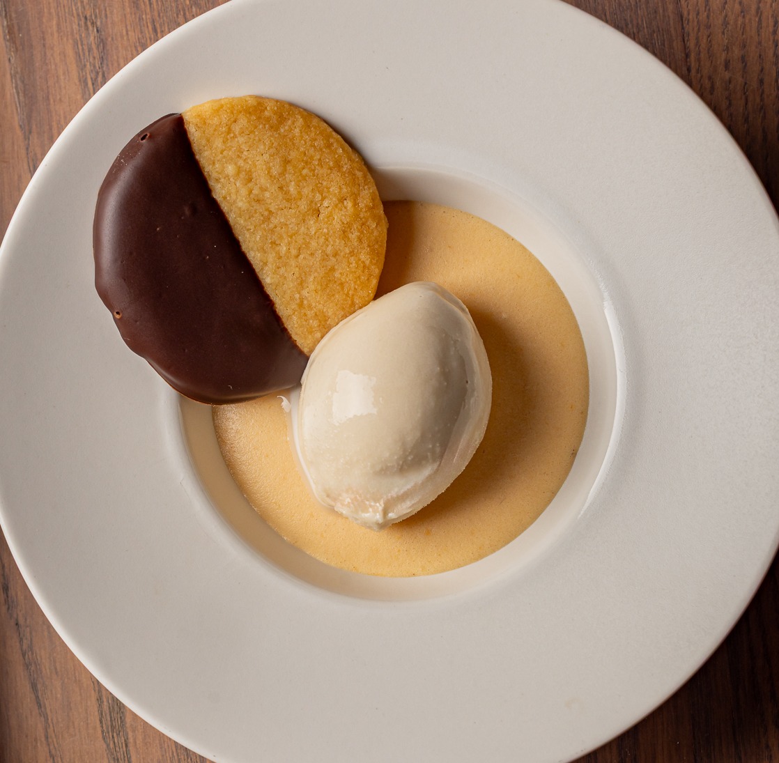 A dessert from a restaurant, there is a half chocolate covered large biscuit and a quenelle of ice cream.