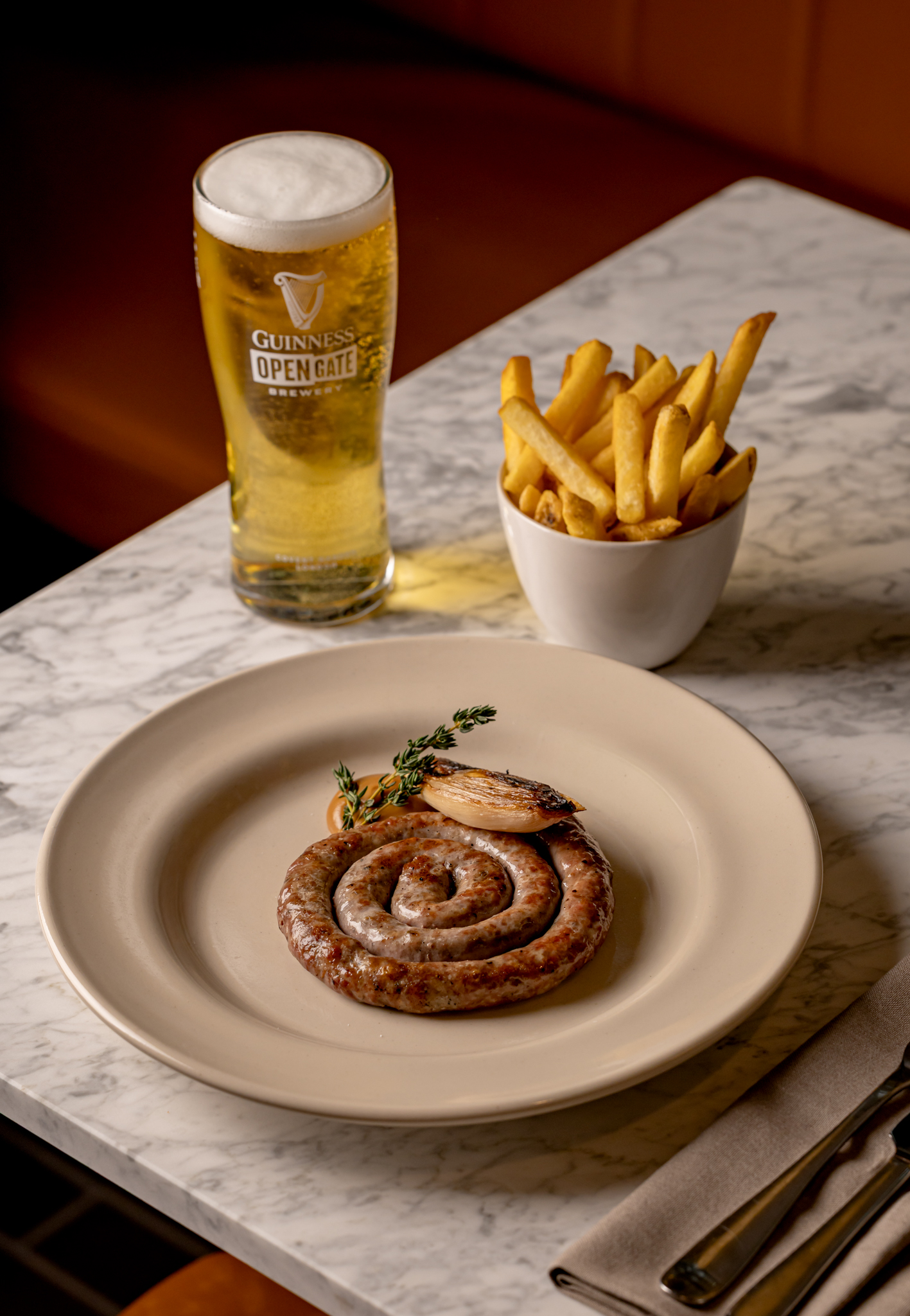 A delicious plate of rolled pork and fennel sausage. Paired with a bowl of crunchy fries and a crisp pint of lager from Open Gate Brewery in London.