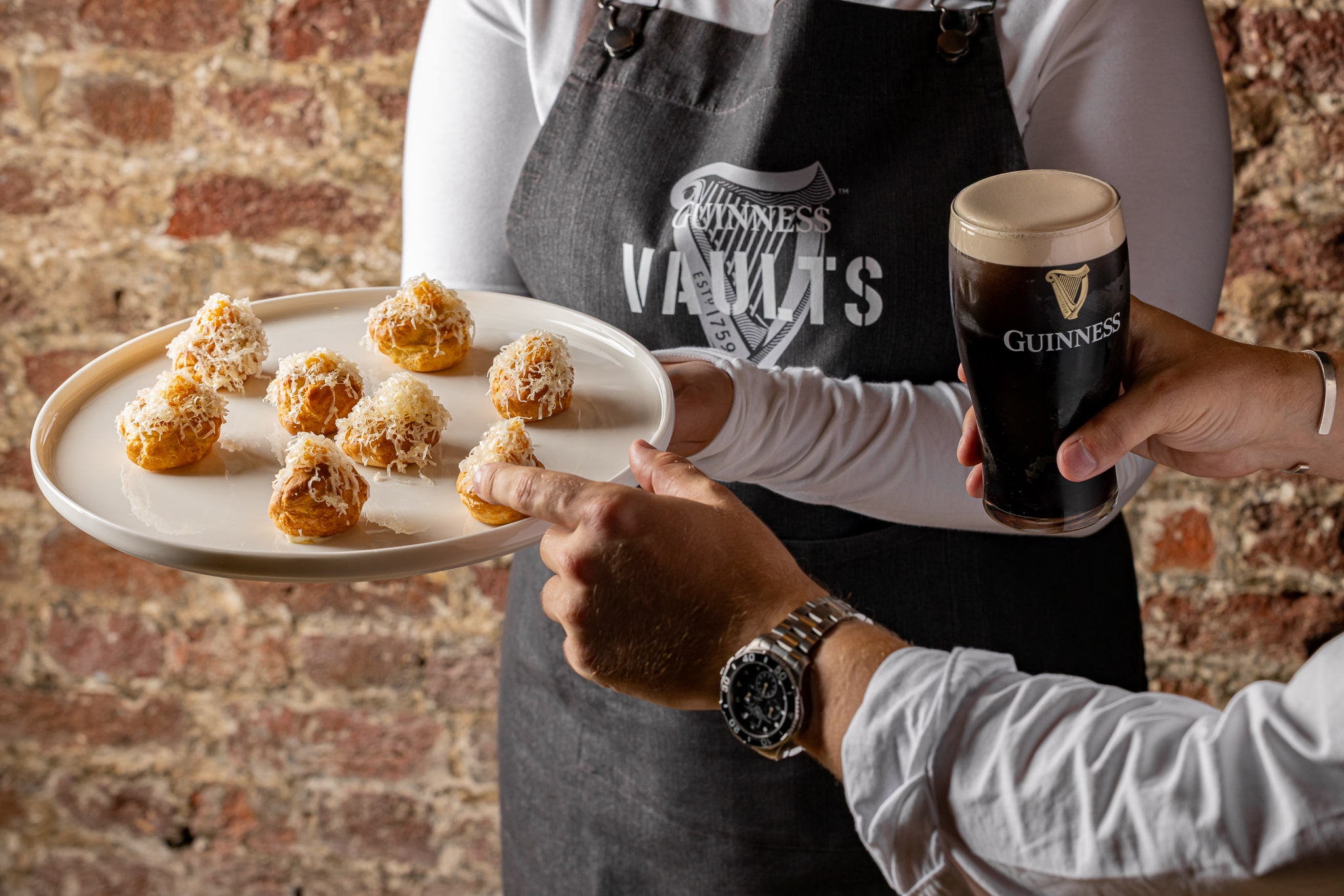 A plate of canapés is held out by a waiter and a hand reaches to take one.