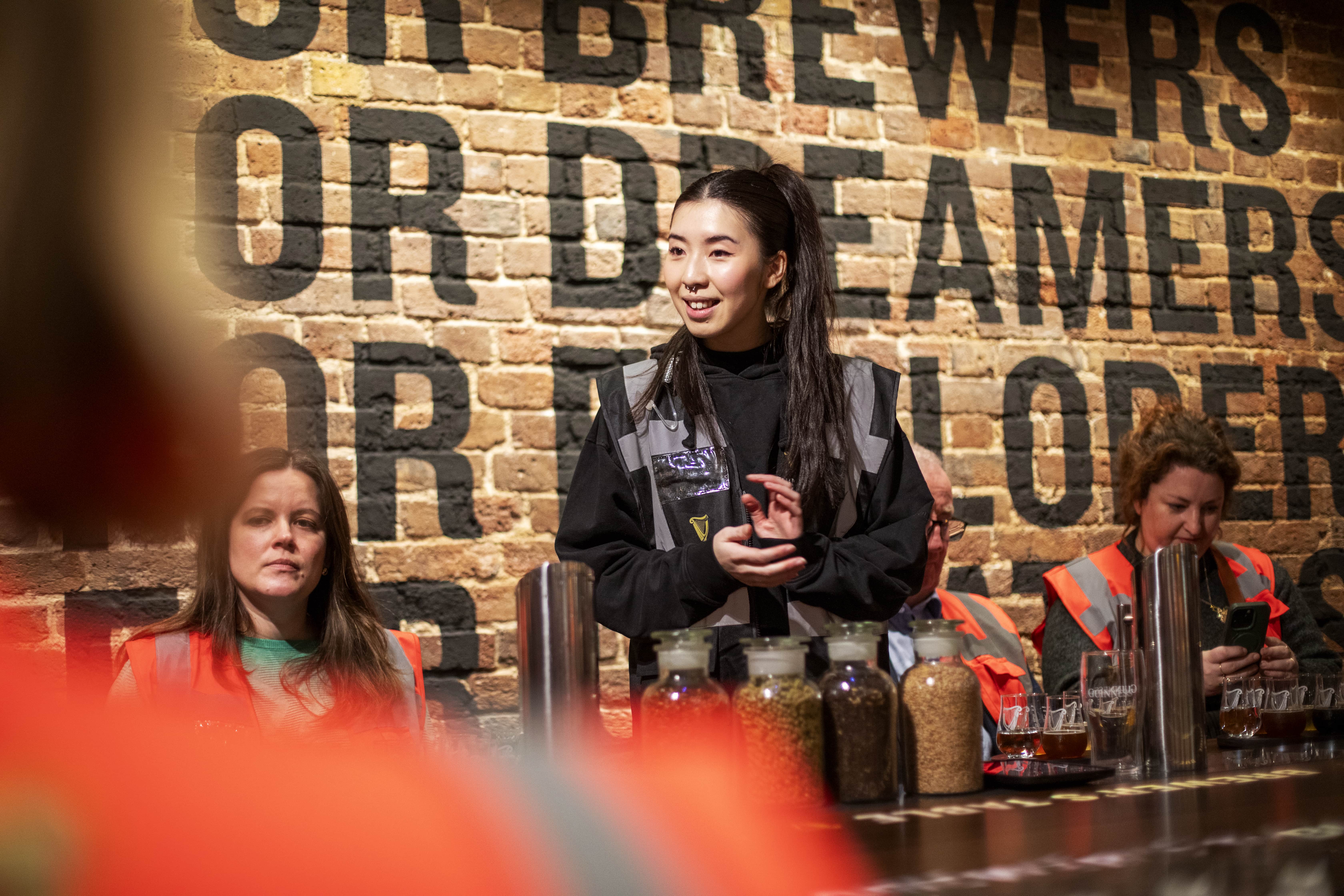 A tour guide stands in the tasting room and talks to a table filled with guests, with jars of smelling ingredients laid on the table.