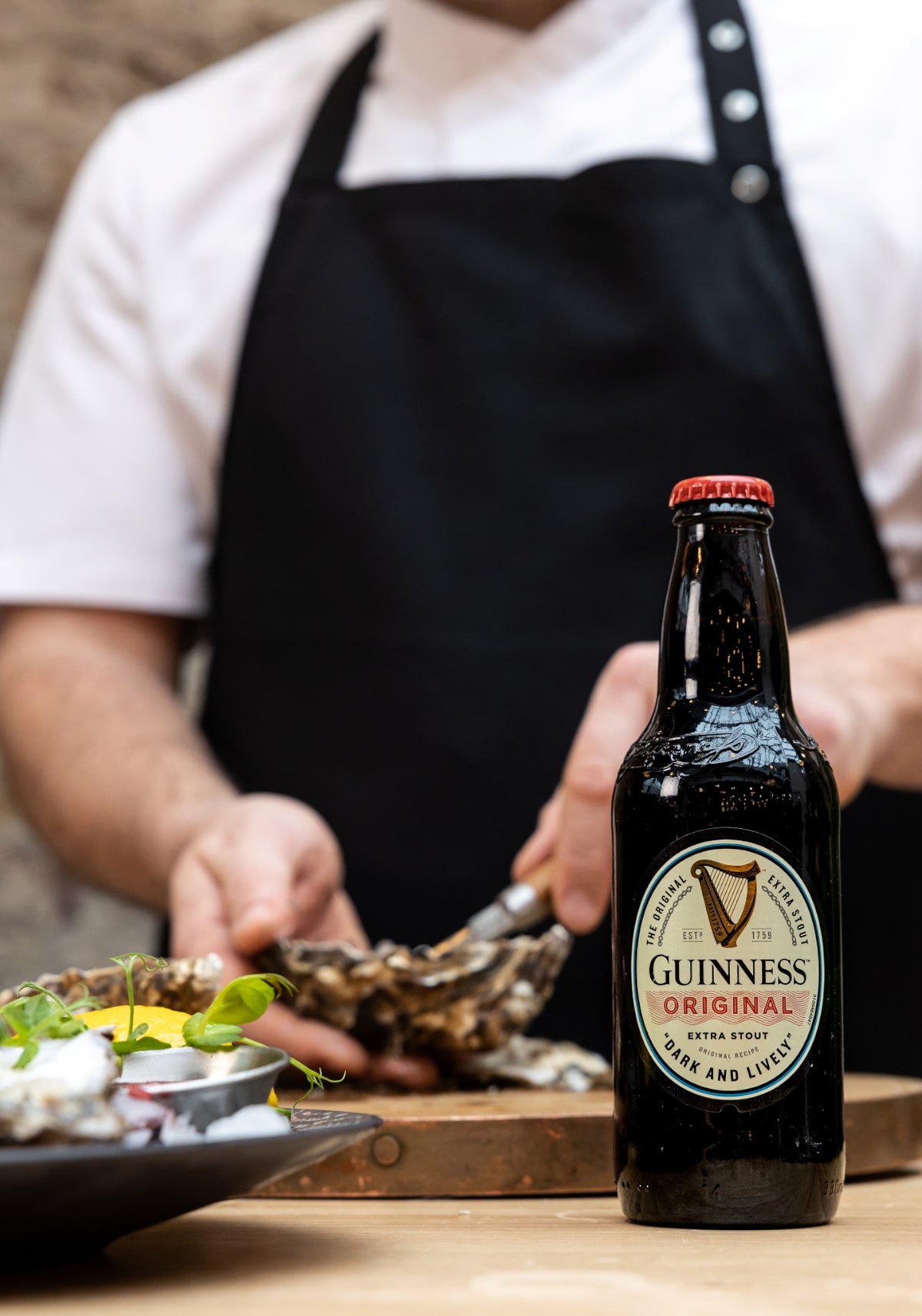 A bottle of Guinness with a chef shucking an oyster in the background.