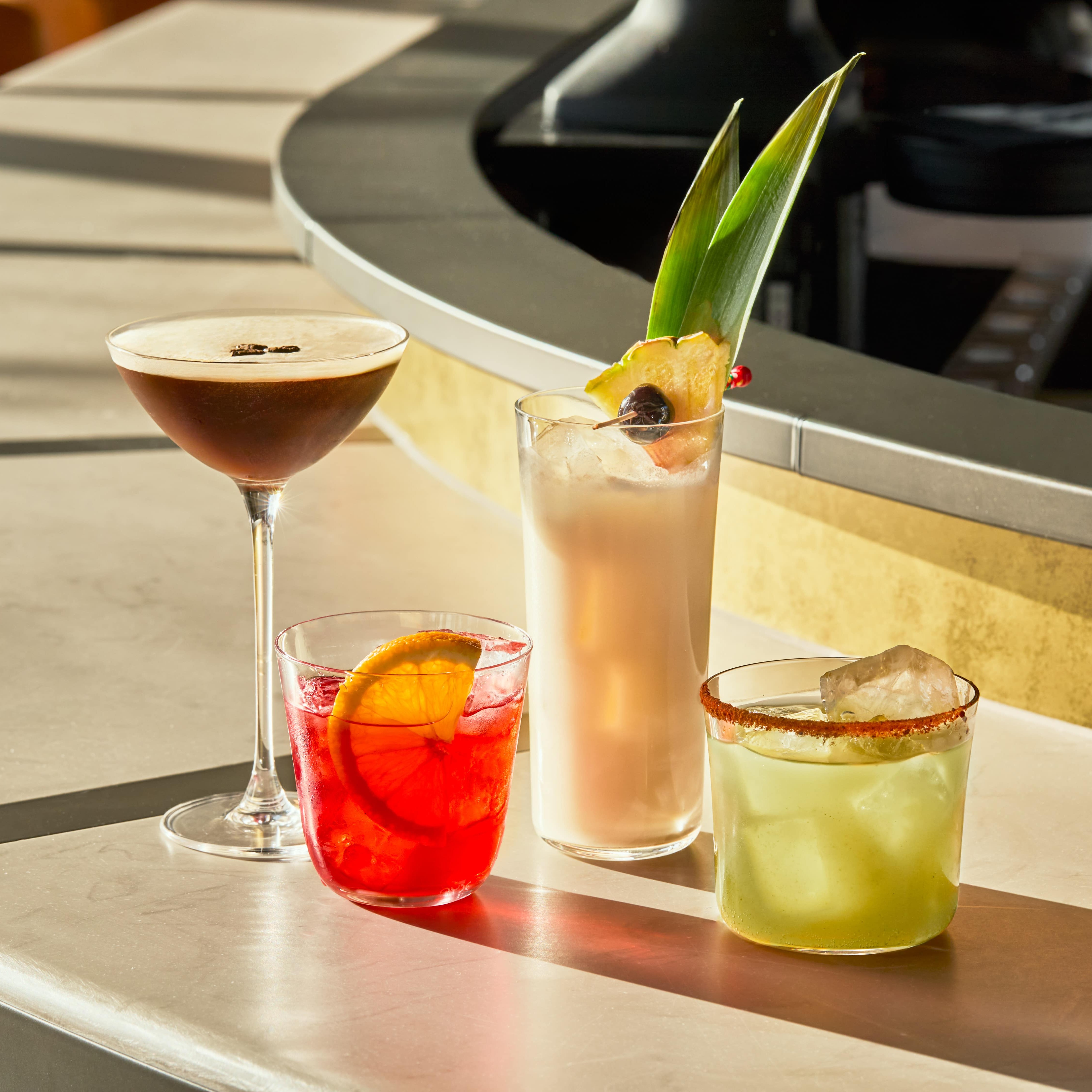 A collection of four cocktails stand in the sunlight on the bar in the rooftop restaurant Gilroy's Loft