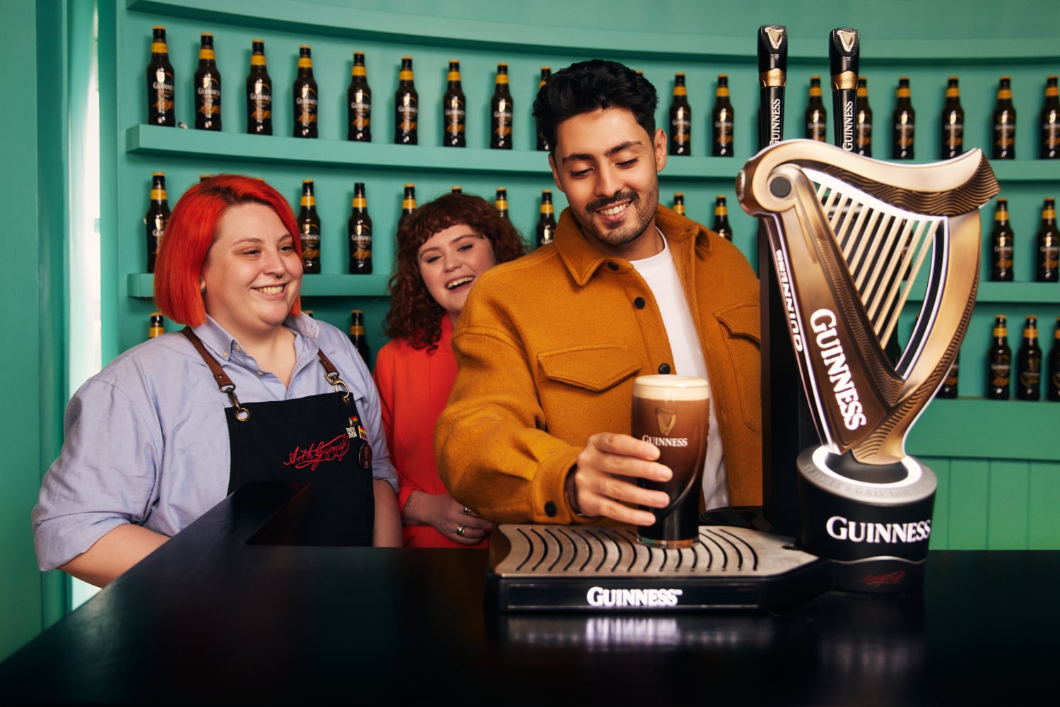 A man in a Guinness shirt holds up a Guinness pint glass and is explaining something to the people standing around him.