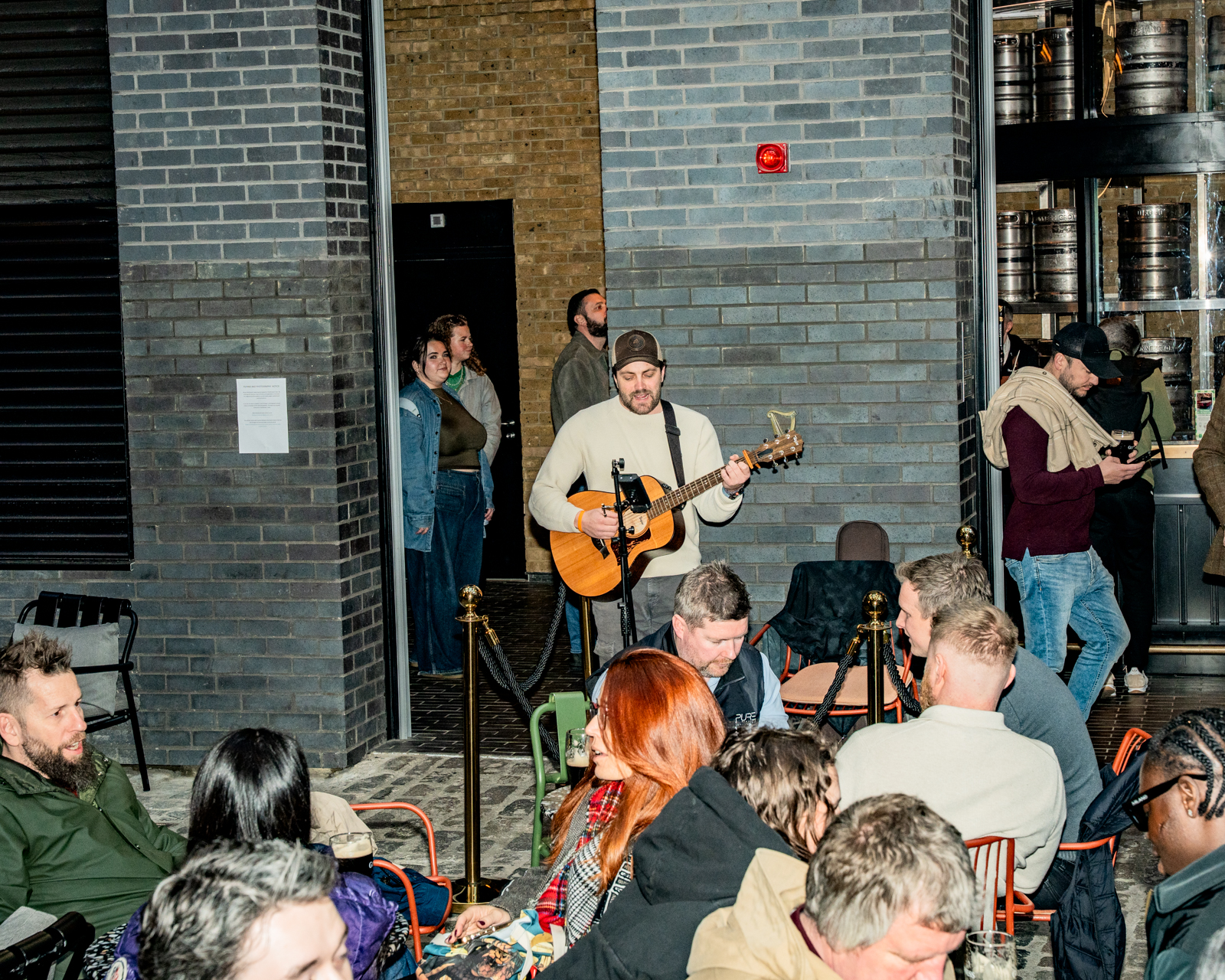 A man with a guitar stands in the centre of our outdoor courtyard bar while the audience enjoys their pints of Guinness and craft beer
