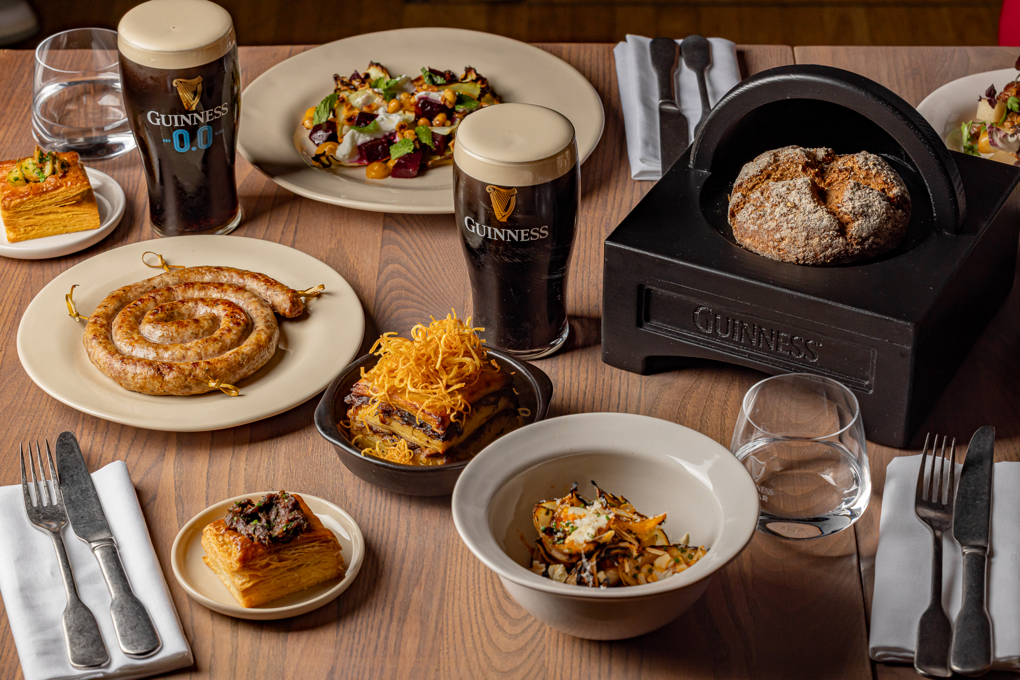 An image of food on a table. Guinness glass with poured Guinness on the middle and the bread in Guinness haversack