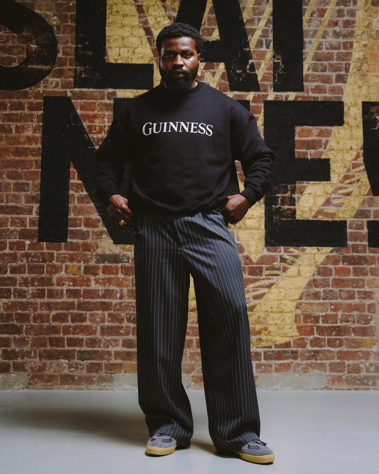 A man wears a black Guinness x Six Nations long sleeved jumper, with text across the front that says Guinness in capital letters.