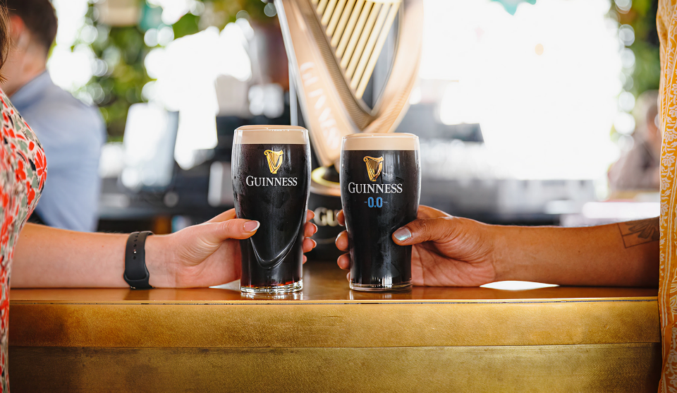 A pint of Guinness and a pint of Guinness 0.0 held next to each other on a bar.