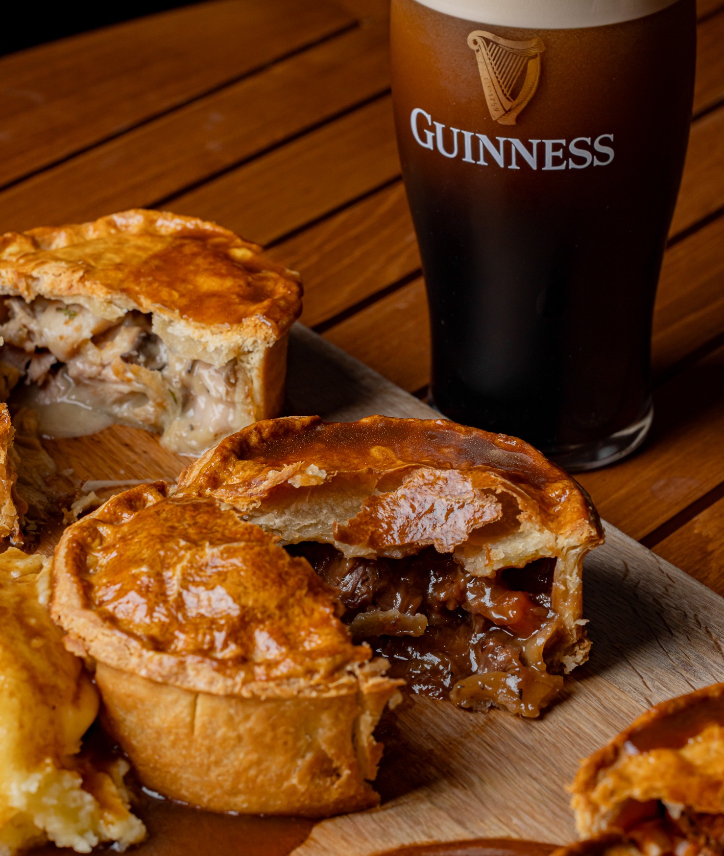Golden-brown pies, some open with savory fillings, on a wooden surface next to a pint of Guinness.