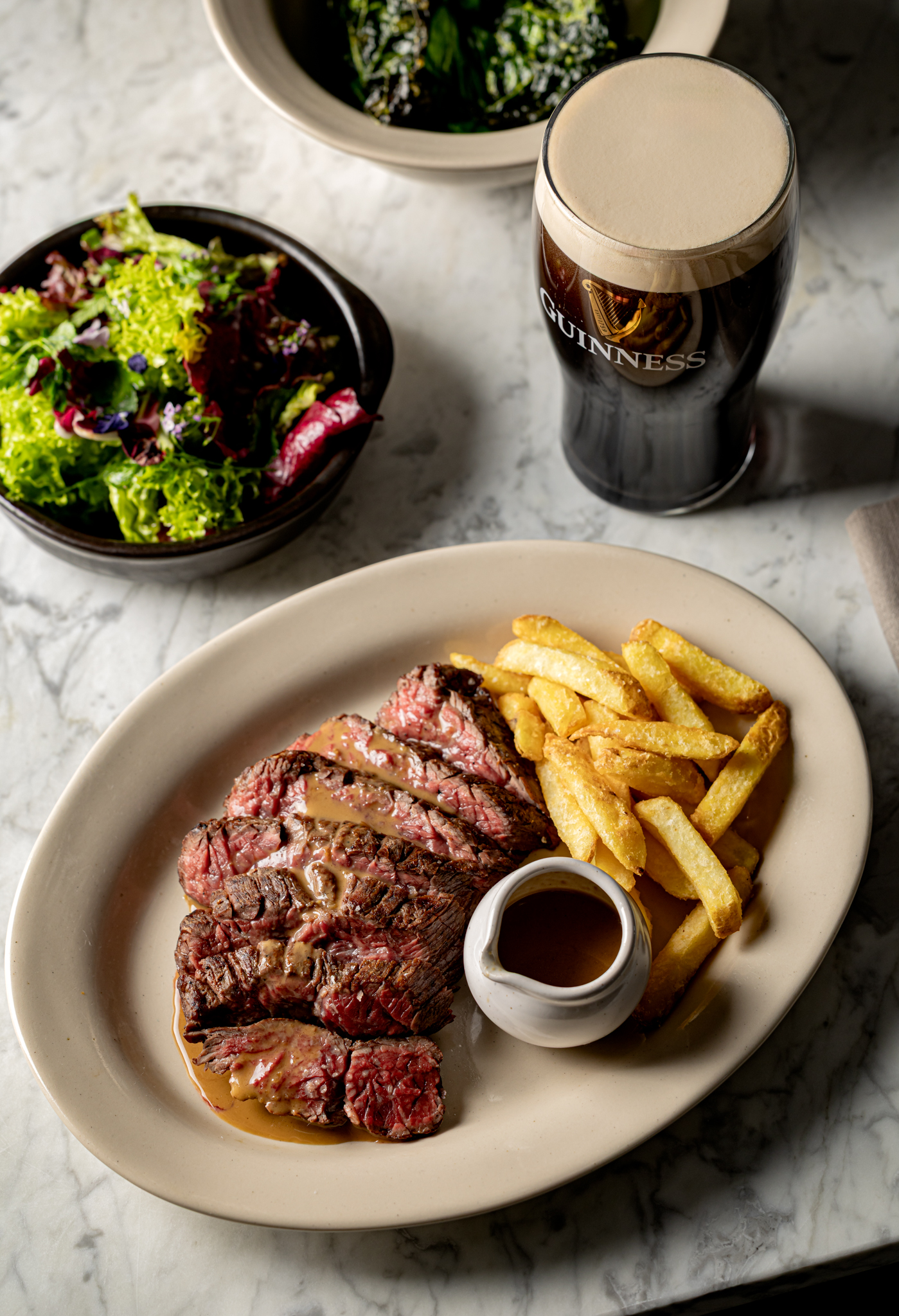 A plate of sliced beef bavette steak and medium-cut chips with Guinness and green peppercorn sauce, perfectly paired with a pint of Guinness.