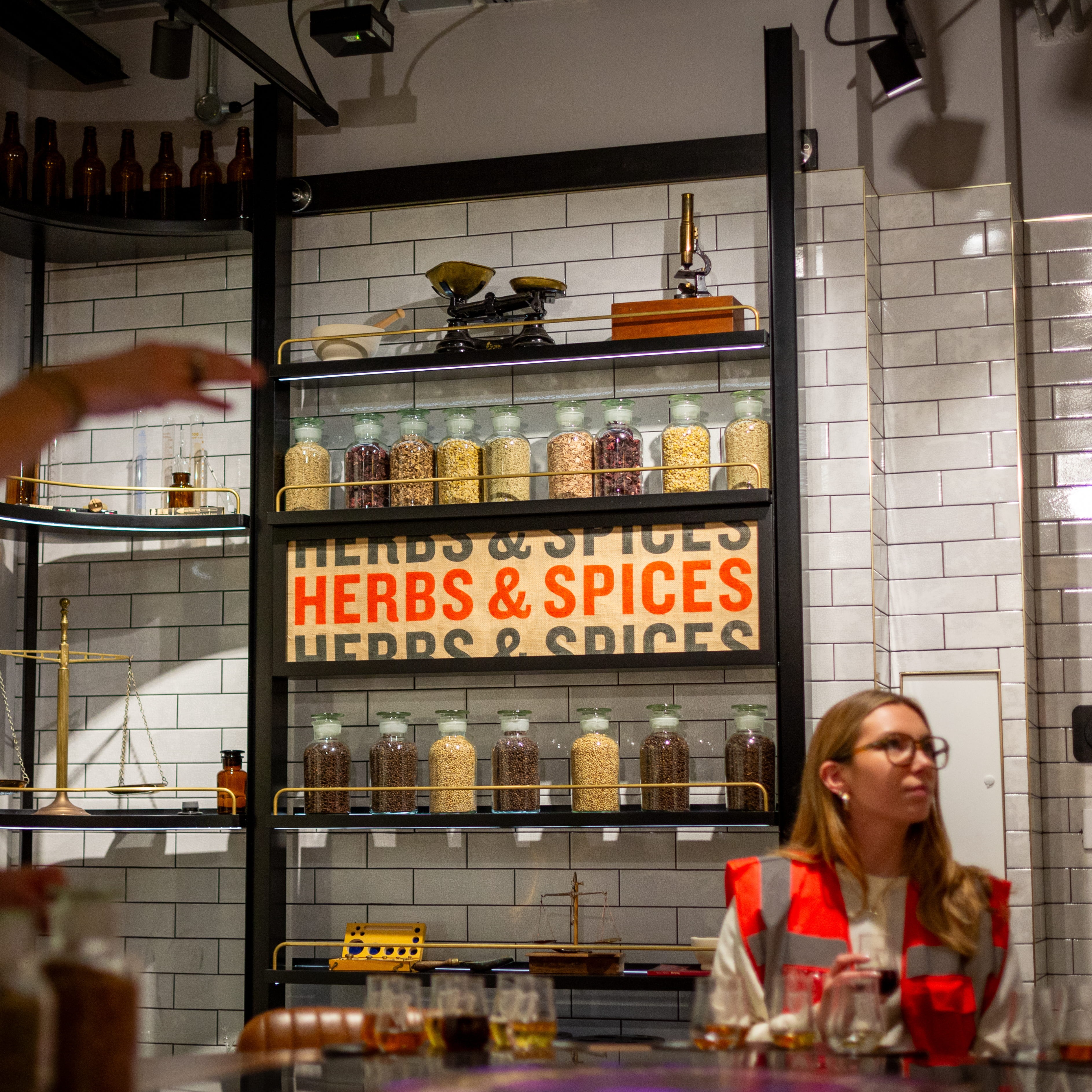 A woman sits in front of shelves filled with ingredients and tasting notes in the beer tasting room on the Open Gate Brewery tour in London