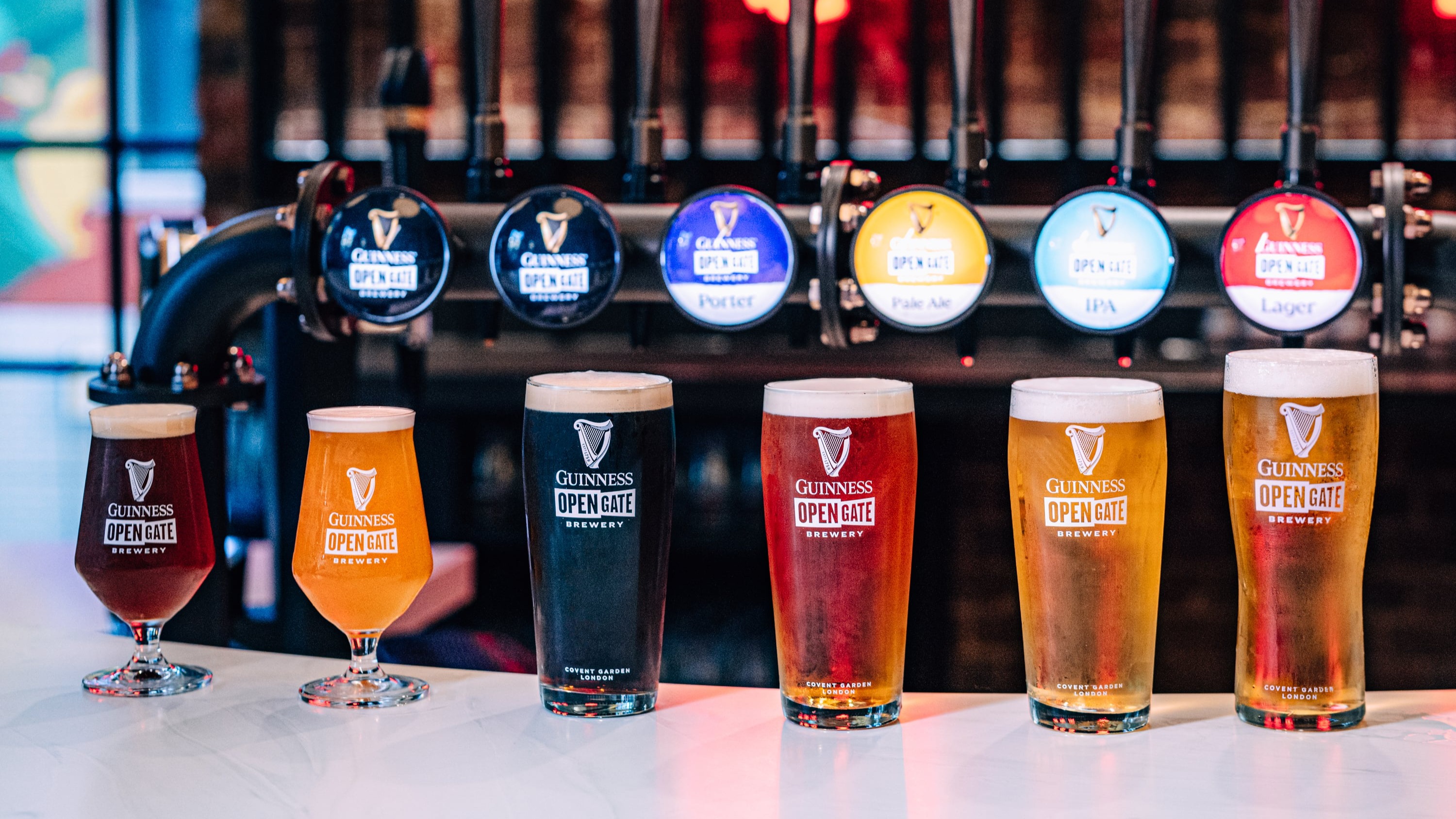 A line of 6 beers on a bar in front of their beer taps
