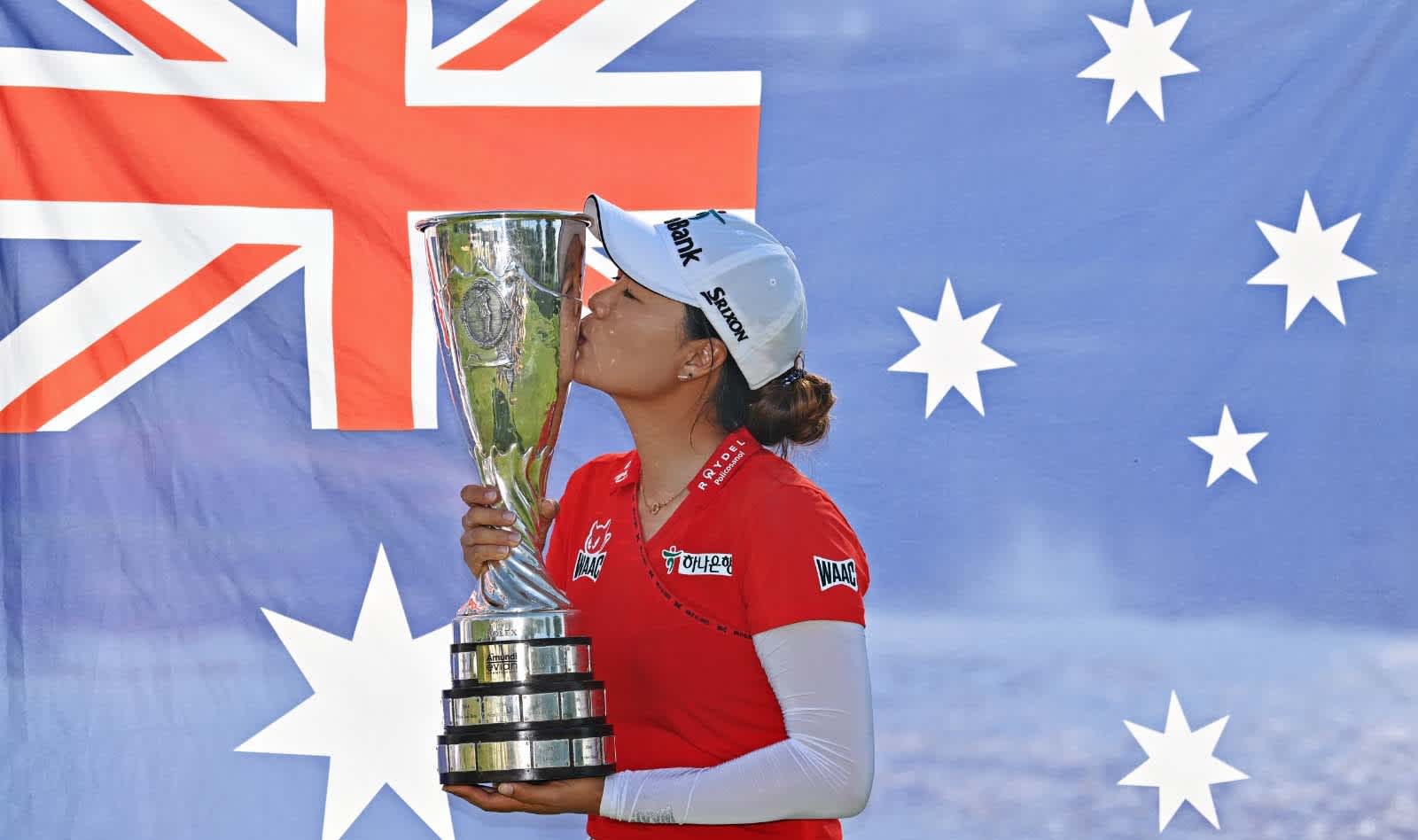 Minjee Lee kisses the Evian Championship trophy in front of the Australian flag.