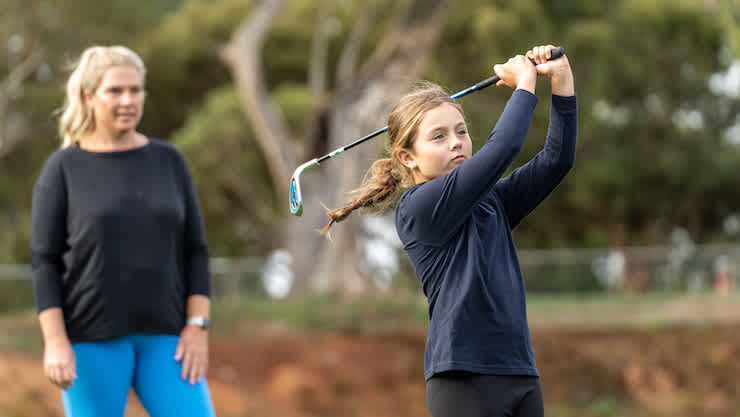 Woman giving a young girl a golf lesson.