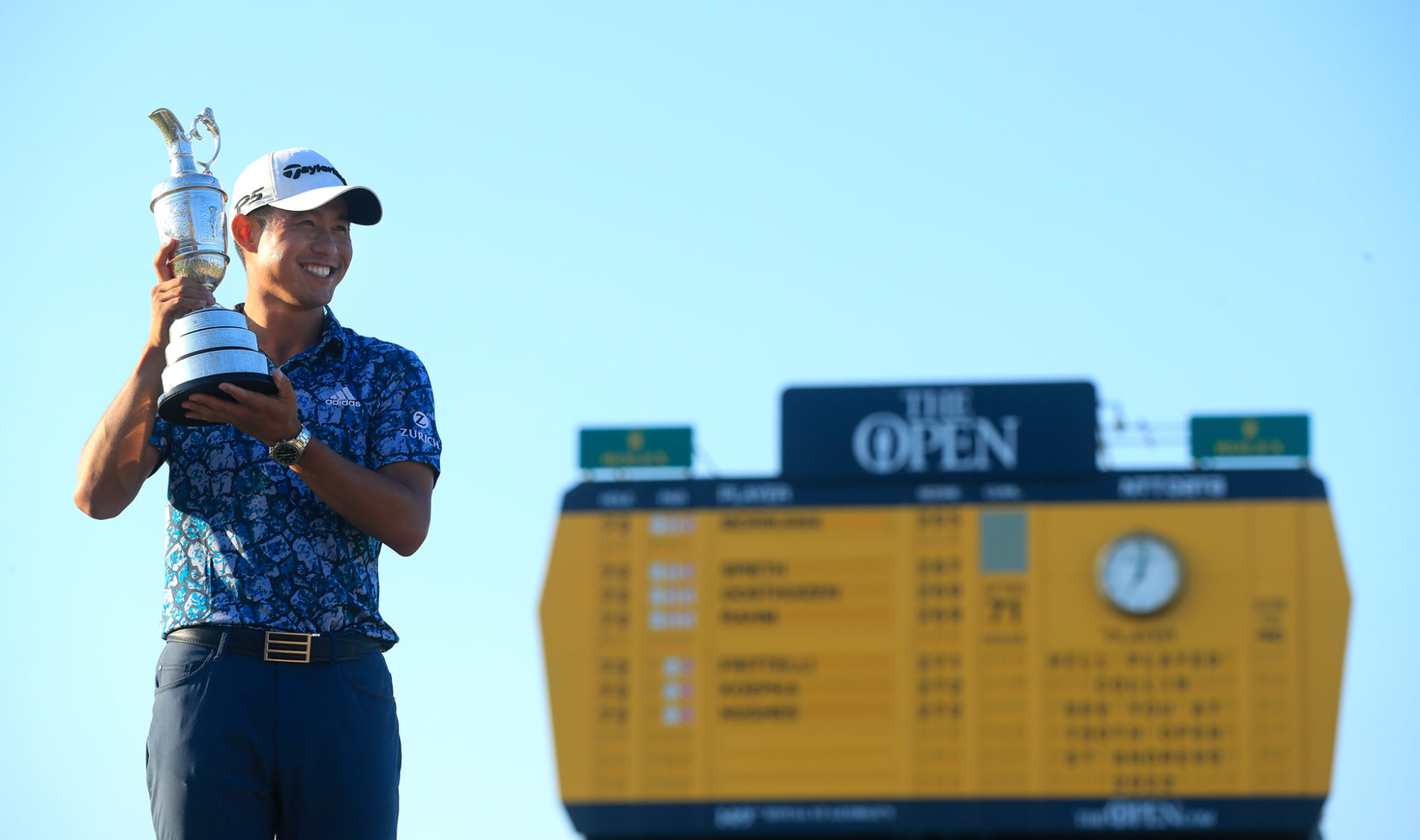 Collin Morikawa holds the Claret Jug in front of the famous yellow scoreboard. 
