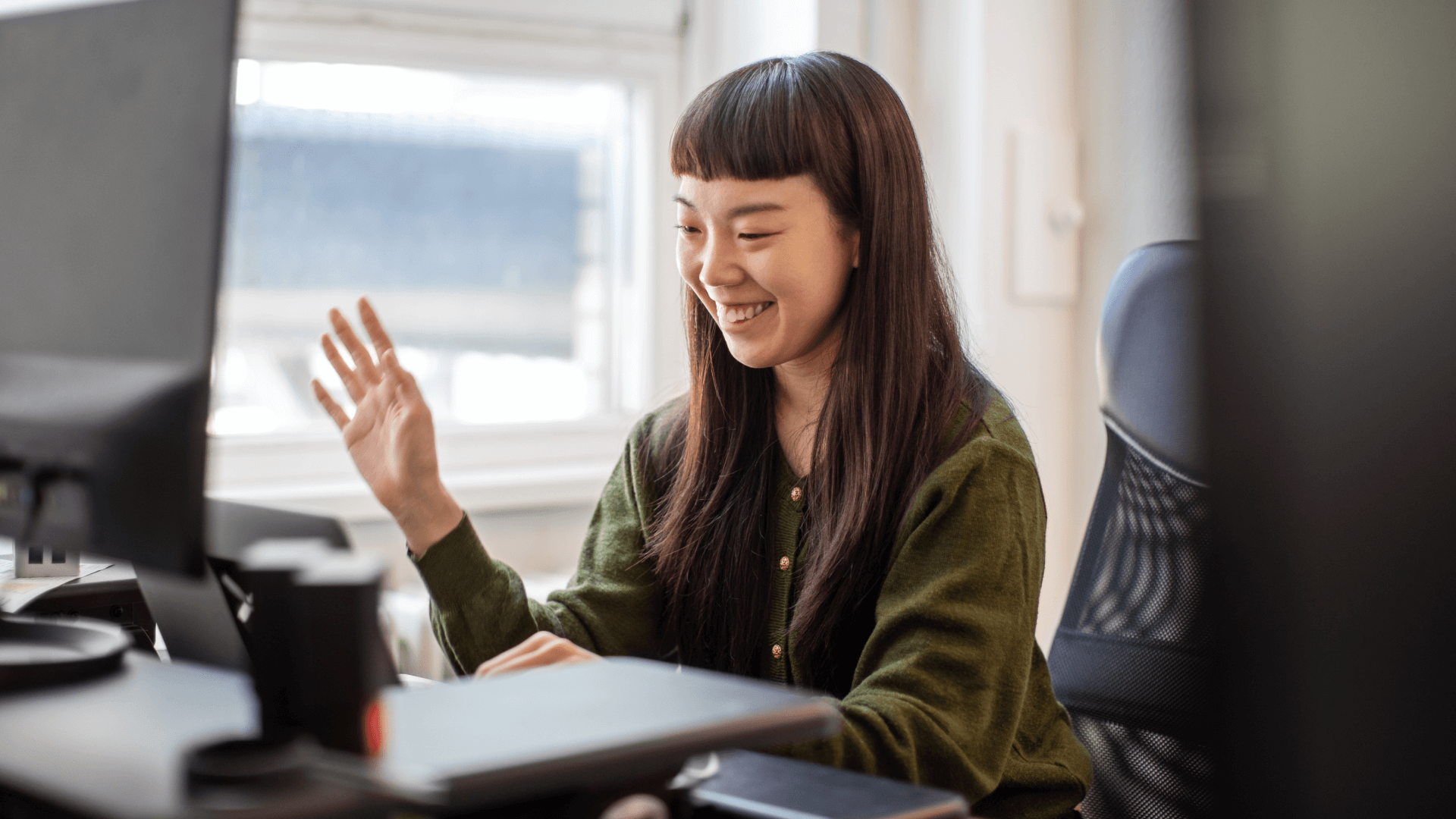 a woman waves at a computer camera