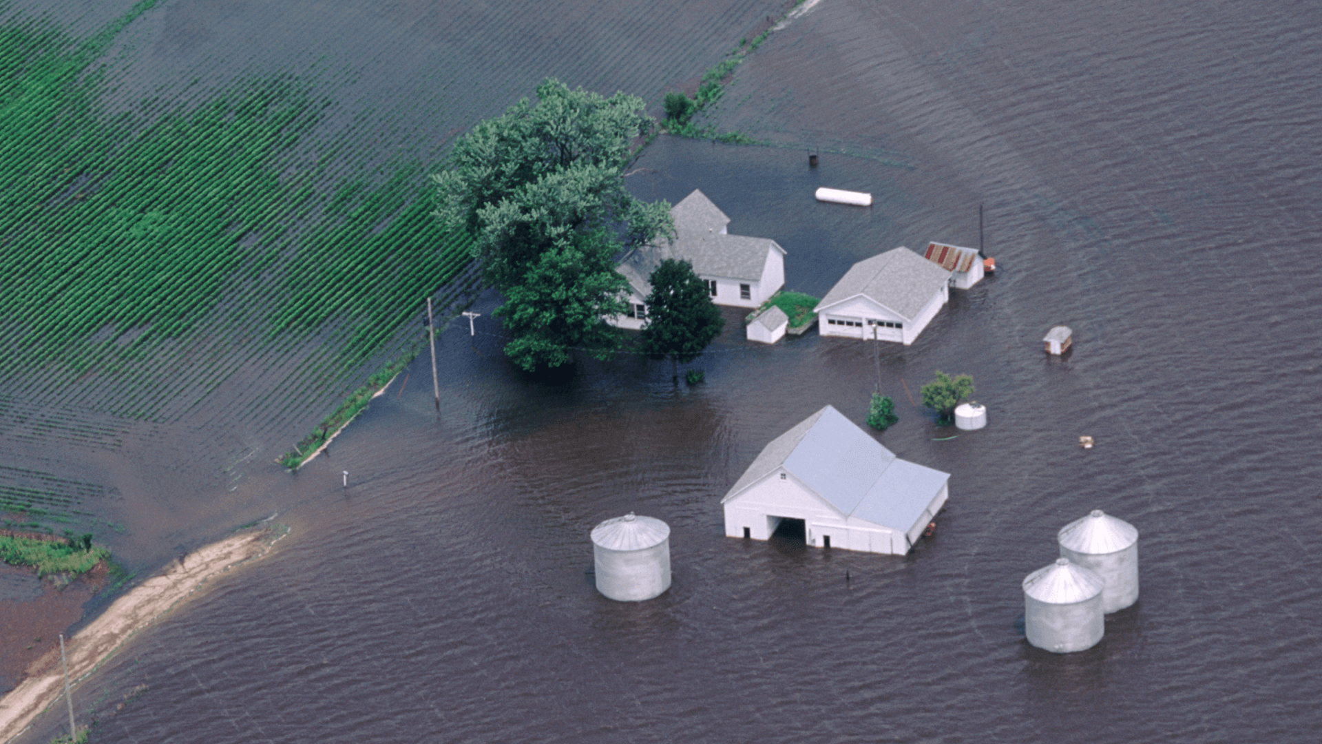 a flooded collection of buildings including a house and barn on a farm